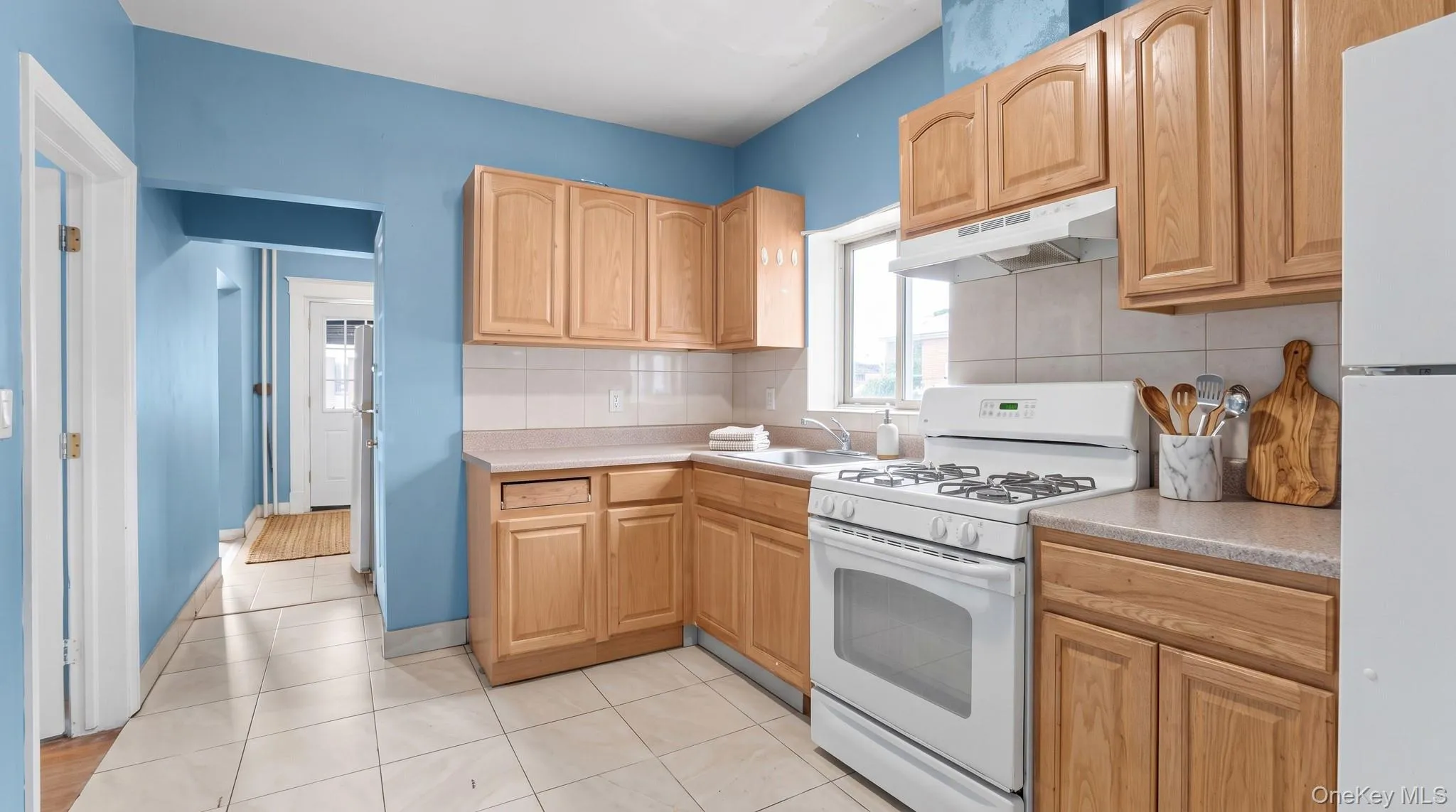 Kitchen featuring wood-finish cabinetry, tile flooring, white appliances, and a window Kitchen featuring wood-finish cabinetry, tile flooring, white appliances, and a window