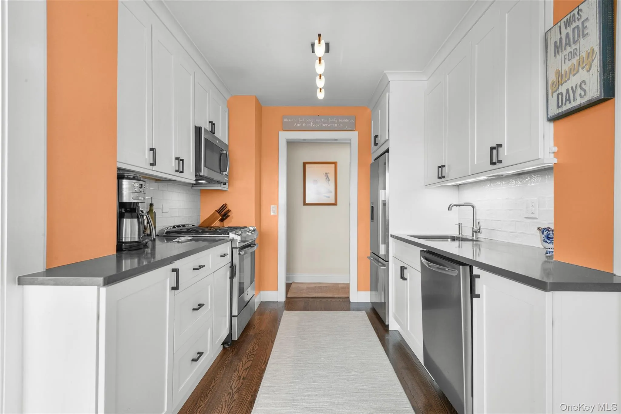 Galley kitchen featuring white cabinetry, dark countertops, and stainless steel appliances Galley kitchen featuring white cabinetry, dark countertops, and stainless steel appliances