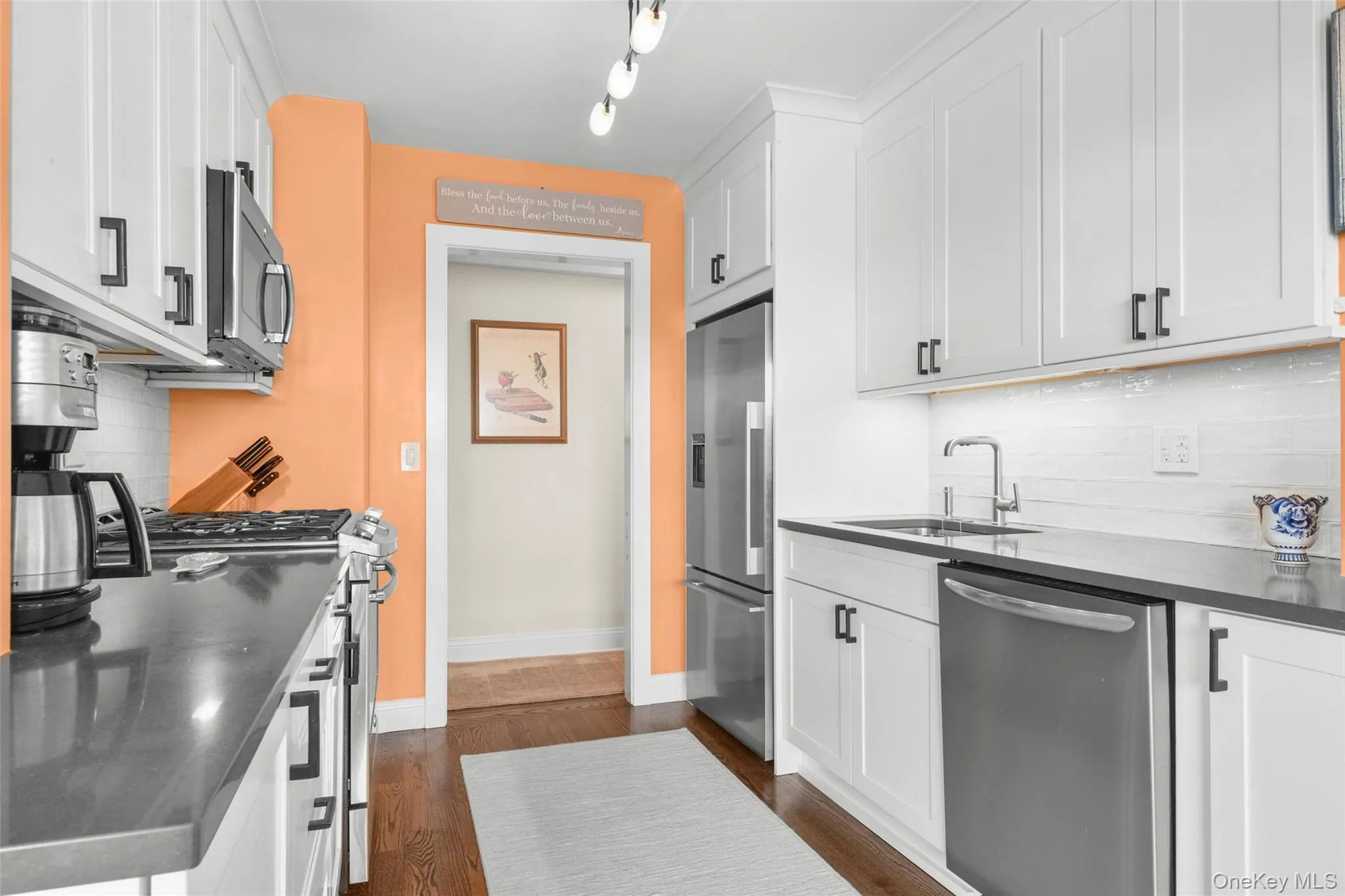 Galley kitchen featuring white cabinetry, dark countertops, and stainless steel appliances Galley kitchen featuring white cabinetry, dark countertops, and stainless steel appliances