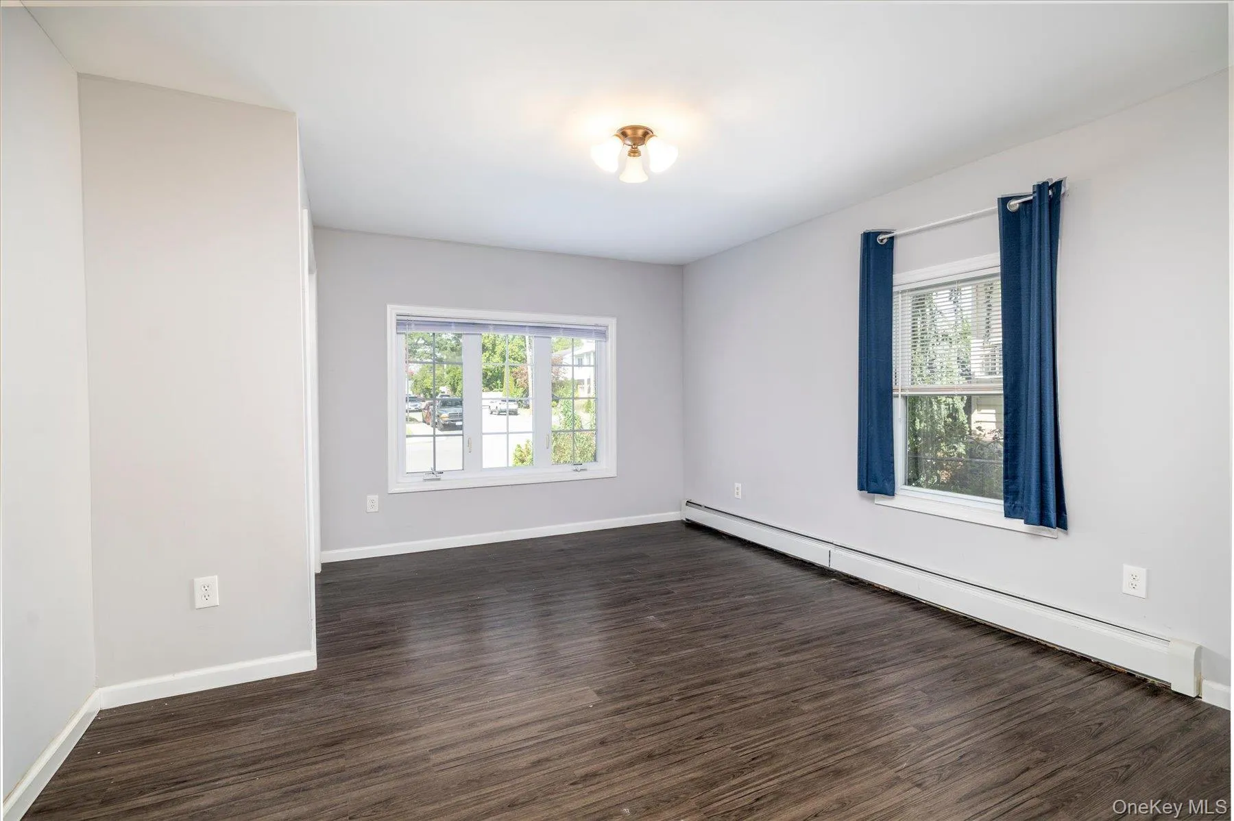Spacious room featuring wood-finish flooring, light grey wall paint, and a multi-pane window Spacious room featuring wood-finish flooring, light grey wall paint, and a multi-pane window