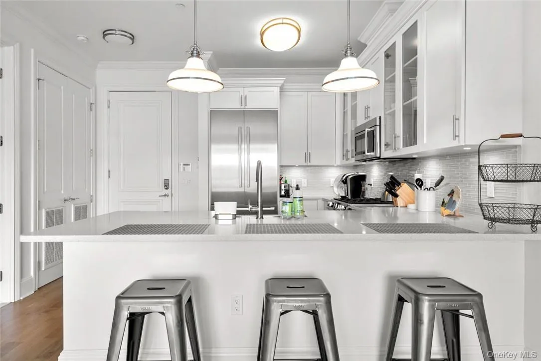 Kitchen with dark hardwood / wood-style flooring, a kitchen breakfast bar, white cabinetry, stainless steel appliances, and pendant lighting Kitchen with dark hardwood / wood-style flooring, a kitchen breakfast bar, white cabinetry, stainless steel appliances, and pendant lighting