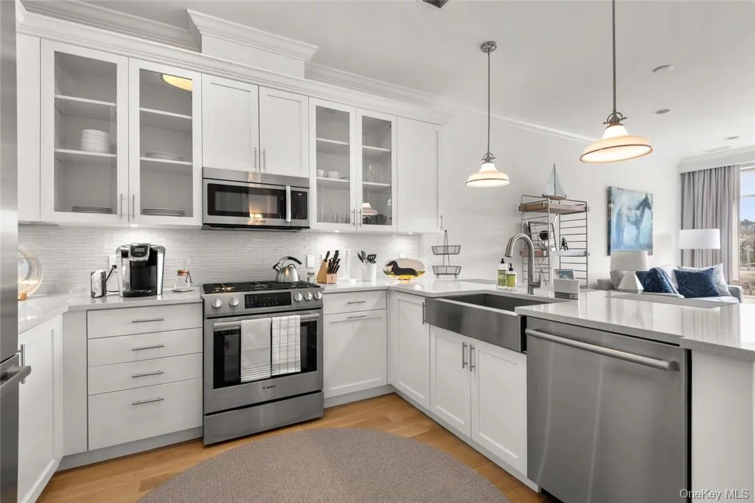 Kitchen with sink, light wood-type flooring, stainless steel appliances, pendant lighting, and white cabinets Kitchen with sink, light wood-type flooring, stainless steel appliances, pendant lighting, and white cabinets