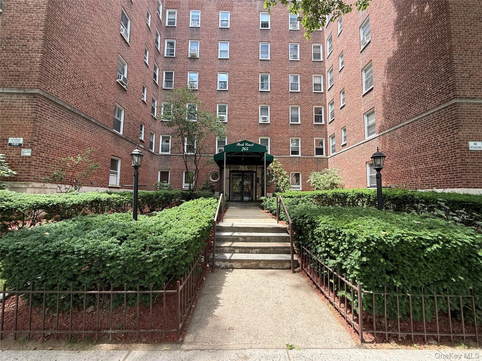 Brick exterior multi-story building featuring a central entrance with a green awning and integrated lighting Brick exterior multi-story building featuring a central entrance with a green awning and integrated lighting