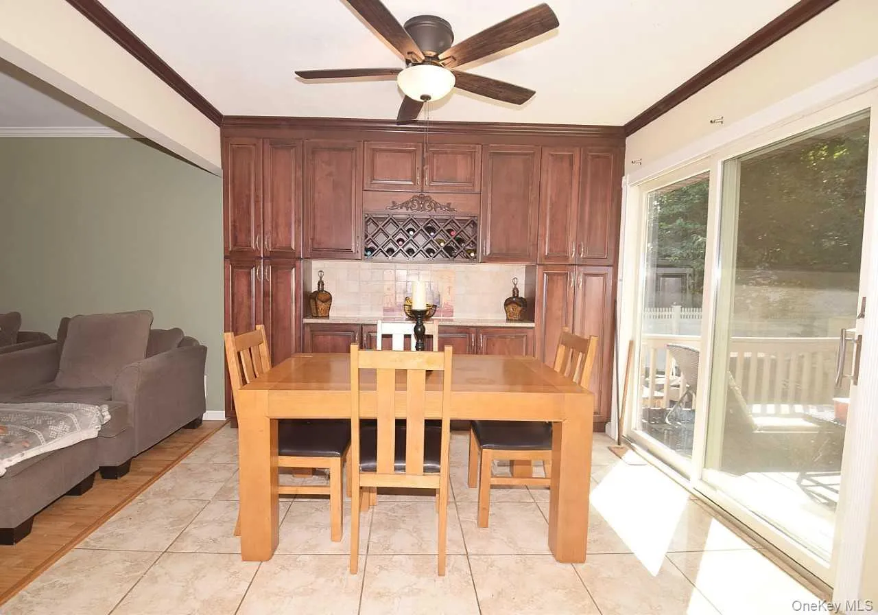 Built-in cabinetry with integrated wine storage, tiled backsplash, ceiling fan with lighting, and sliding glass door to exterior Built-in cabinetry with integrated wine storage, tiled backsplash, ceiling fan with lighting, and sliding glass door to exterior