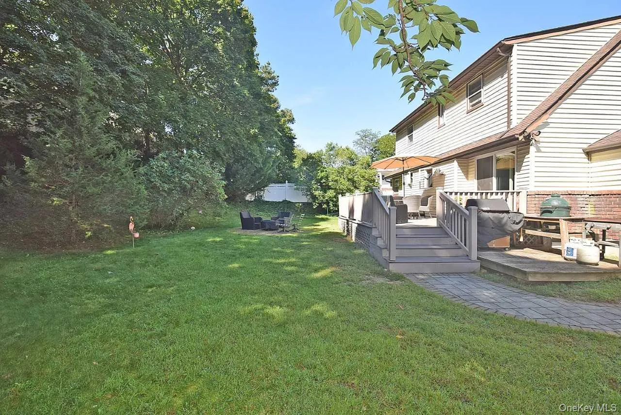 Expansive backyard featuring a manicured lawn, a multi-level deck with steps, a paver walkway, and mature trees providing natural privacy Expansive backyard featuring a manicured lawn, a multi-level deck with steps, a paver walkway, and mature trees providing natural privacy