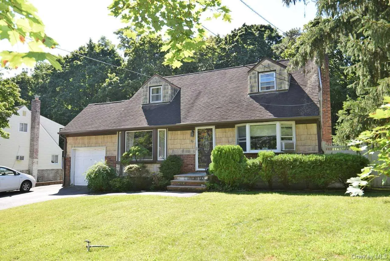 Shingle siding exterior with brick accents, dormer windows, a paved driveway, and established front landscaping Shingle siding exterior with brick accents, dormer windows, a paved driveway, and established front landscaping