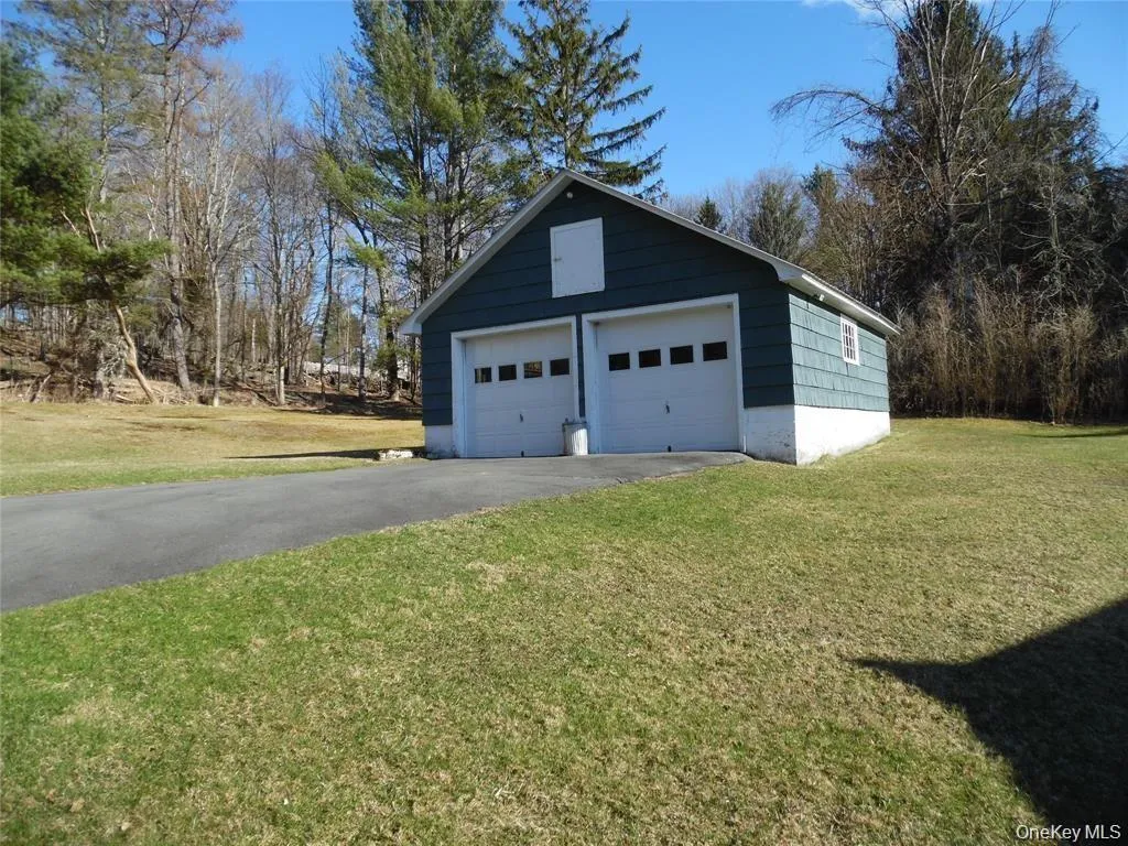 Detached two-car garage with white paneled doors, blue siding, a white foundation, and a pitched roof Detached two-car garage with white paneled doors, blue siding, a white foundation, and a pitched roof