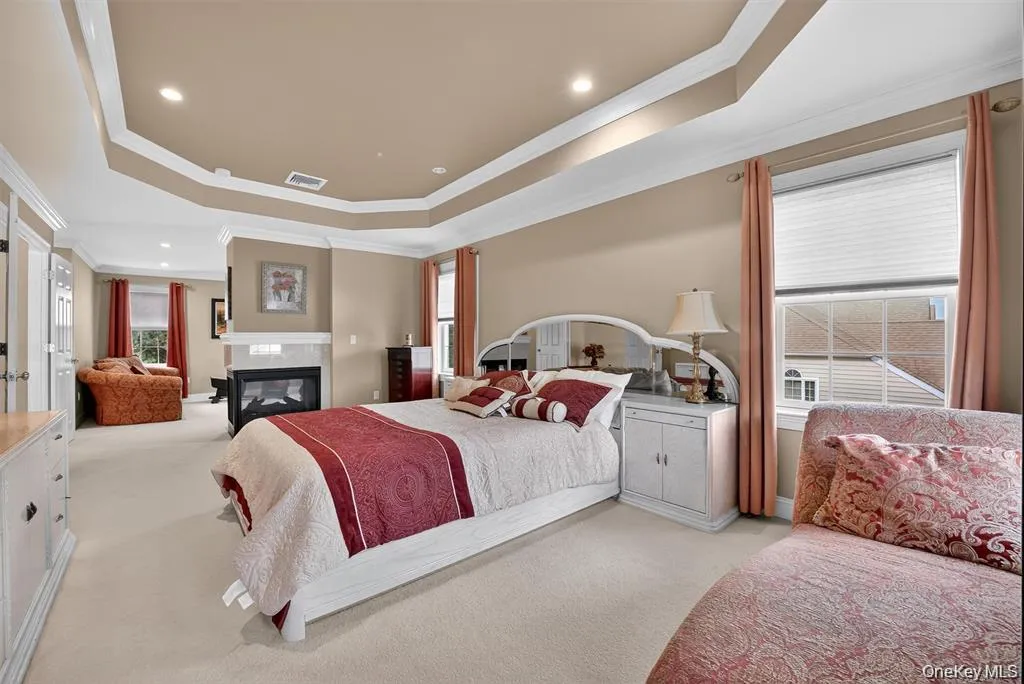 Tray ceiling with recessed lighting, integrated fireplace with stone surround, wall-mounted television, and multiple windows with blinds Tray ceiling with recessed lighting, integrated fireplace with stone surround, wall-mounted television, and multiple windows with blinds