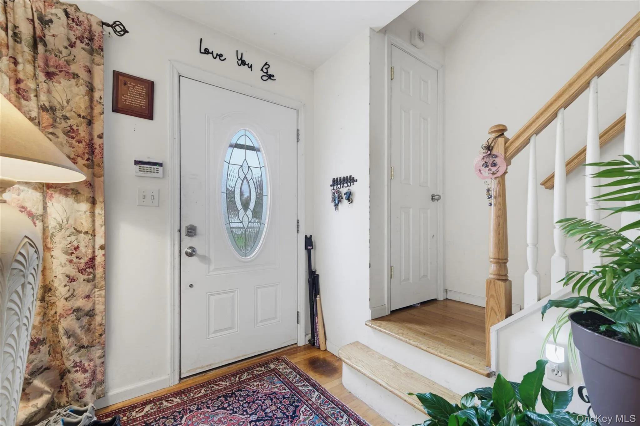 Entryway featuring a white door with an oval decorative glass insert, wood-finish flooring, a wood banister, and white balusters Entryway featuring a white door with an oval decorative glass insert, wood-finish flooring, a wood banister, and white balusters