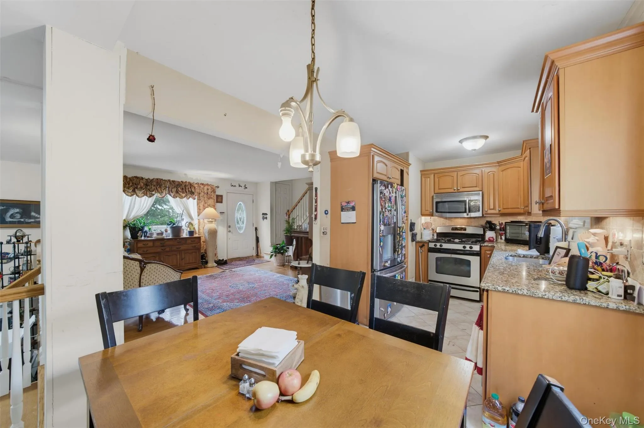 Kitchen and dining area featuring wood cabinetry, granite-style countertops, stainless steel appliances, and a polished wood dining table Kitchen and dining area featuring wood cabinetry, granite-style countertops, stainless steel appliances, and a polished wood dining table