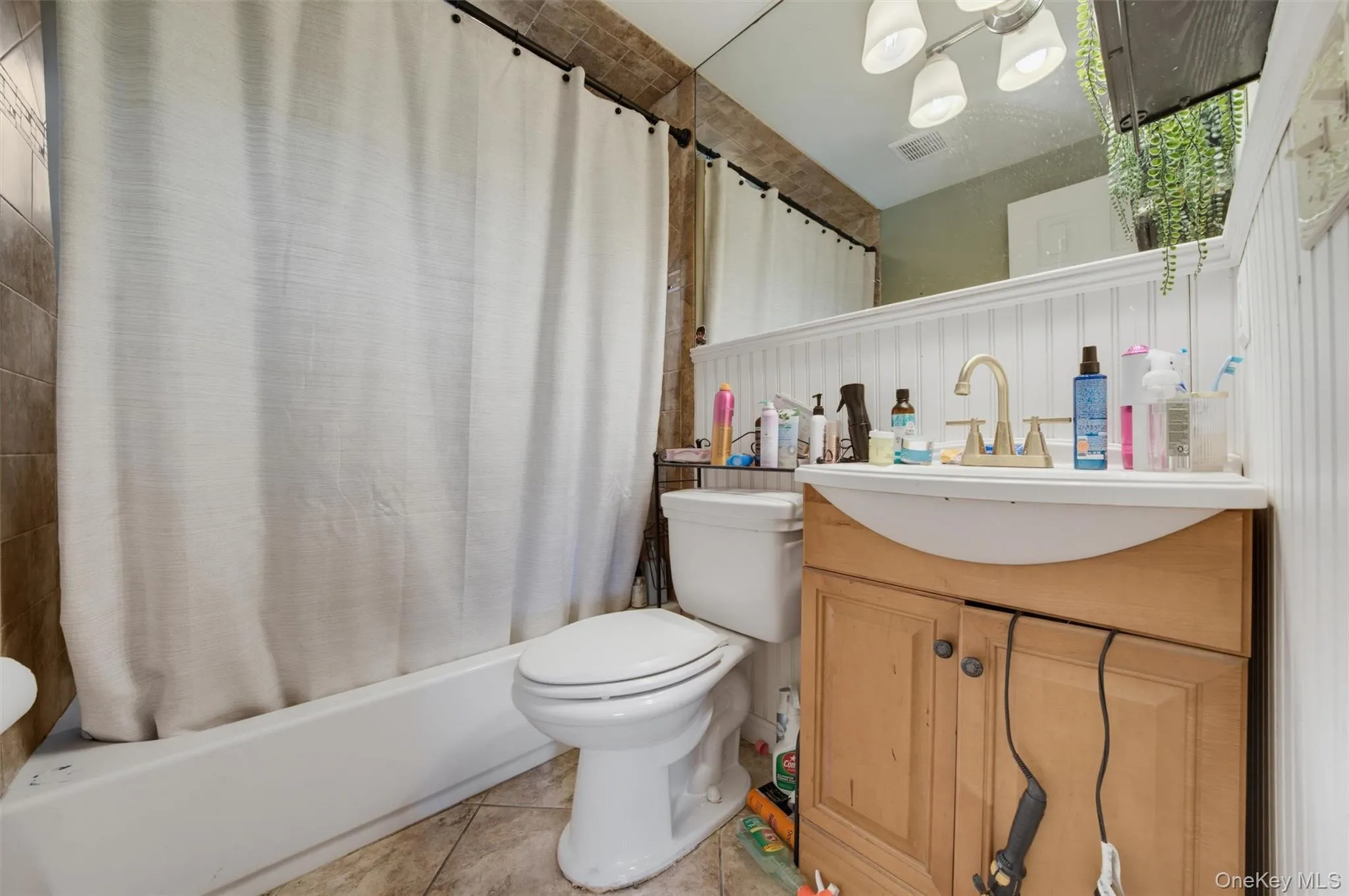 Beige tile wall and floor, white beadboard paneling, light wood-finish vanity, and a white bathtub Beige tile wall and floor, white beadboard paneling, light wood-finish vanity, and a white bathtub