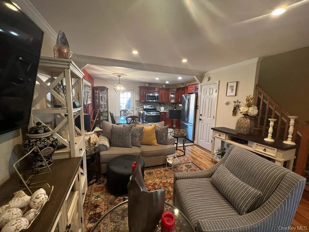 Wood-finish flooring throughout, recessed ceiling lighting, a staircase with wood railings, and a full kitchen with stainless steel appliances Wood-finish flooring throughout, recessed ceiling lighting, a staircase with wood railings, and a full kitchen with stainless steel appliances