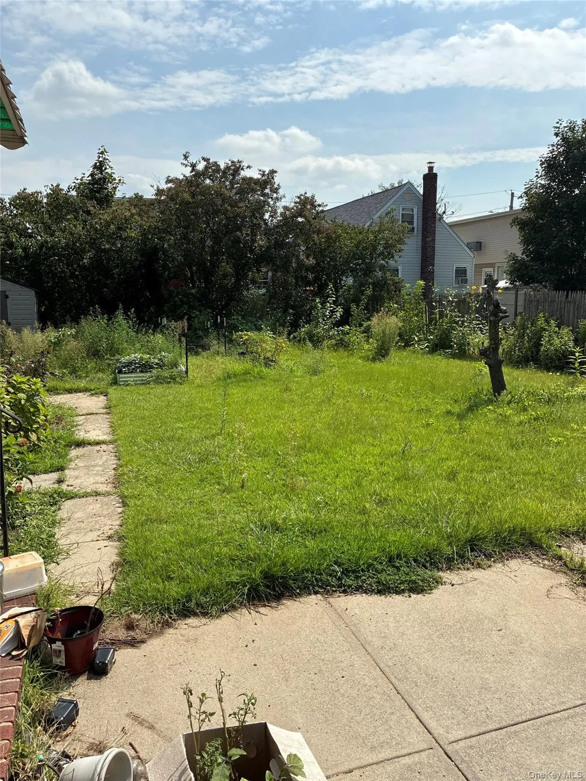 Expansive grassy yard with mature perimeter trees, a concrete patio, and a stone walkway Expansive grassy yard with mature perimeter trees, a concrete patio, and a stone walkway