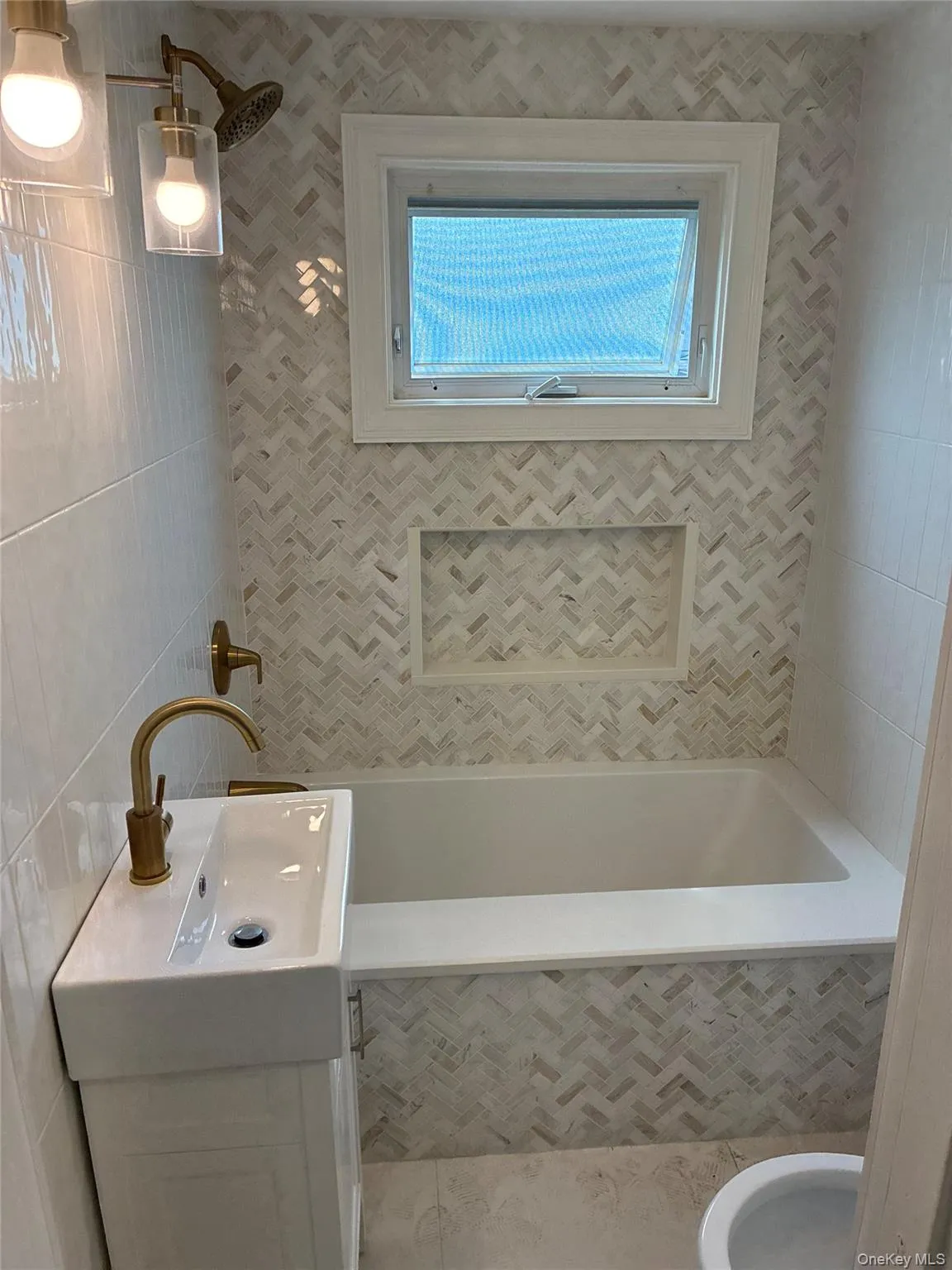 White subway tile walls, herringbone mosaic tile, built-in shower niche, white soaking tub, and brass fixtures White subway tile walls, herringbone mosaic tile, built-in shower niche, white soaking tub, and brass fixtures