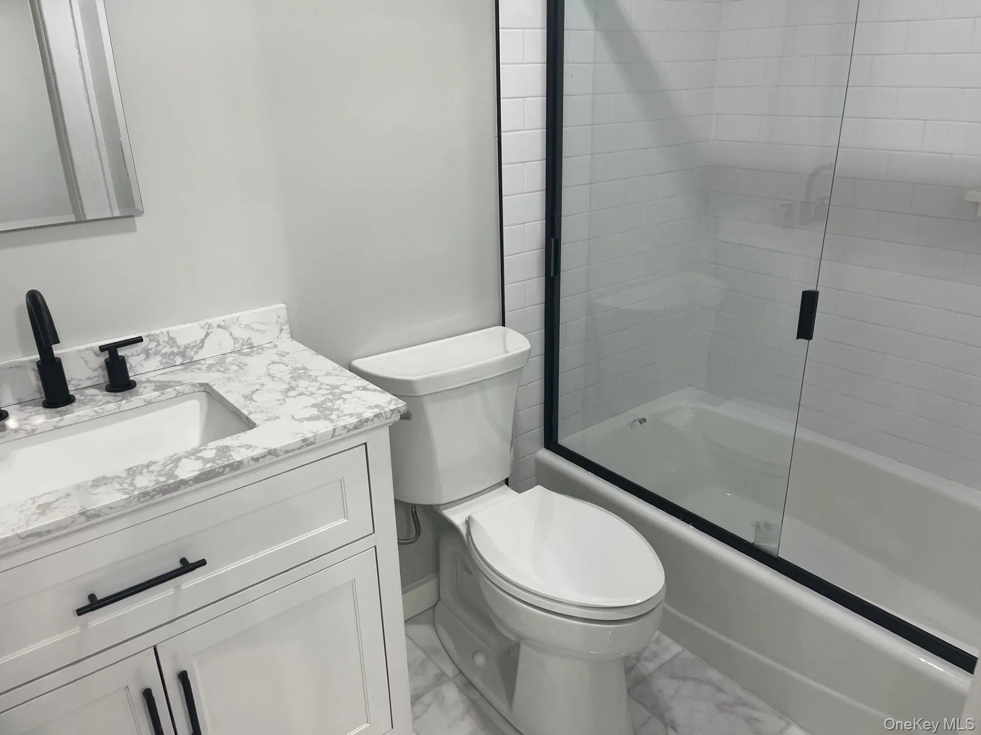 Bathroom featuring enclosed tub / shower combo, vanity, and light marble finish flooring Bathroom featuring enclosed tub / shower combo, vanity, and light marble finish flooring