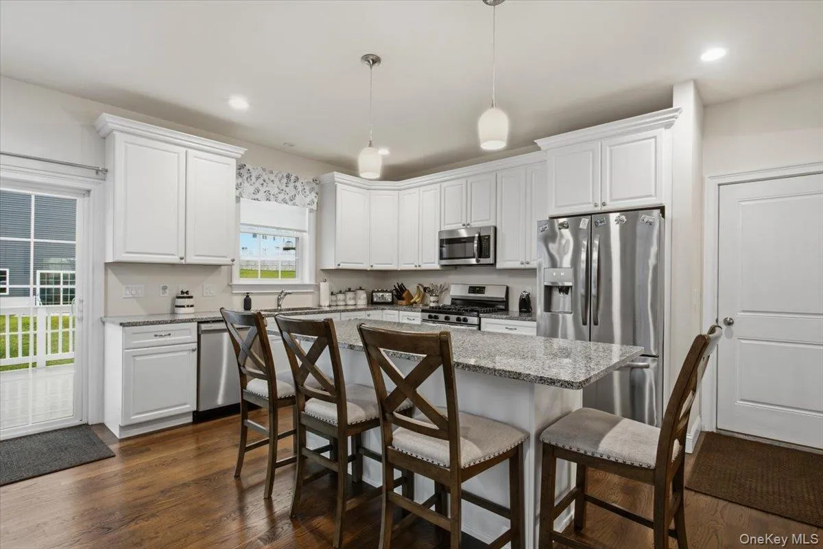 Kitchen featuring white cabinetry, stainless steel appliances, a center island with seating, pendant lighting, and wood-finish flooring Kitchen featuring white cabinetry, stainless steel appliances, a center island with seating, pendant lighting, and wood-finish flooring