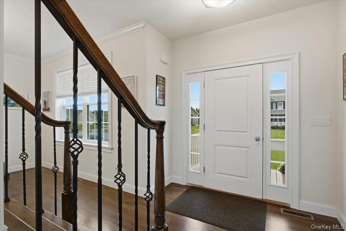 Entryway featuring a white paneled door with glass sidelights, wood-finish flooring, and a staircase with an iron spindle railing Entryway featuring a white paneled door with glass sidelights, wood-finish flooring, and a staircase with an iron spindle railing