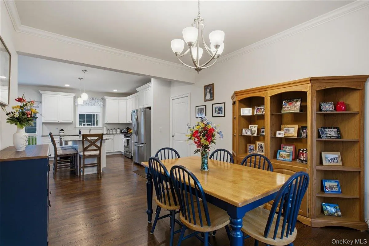 Hardwood flooring, crown molding, white kitchen cabinetry, stainless steel appliances, and a built-in shelving unit Hardwood flooring, crown molding, white kitchen cabinetry, stainless steel appliances, and a built-in shelving unit