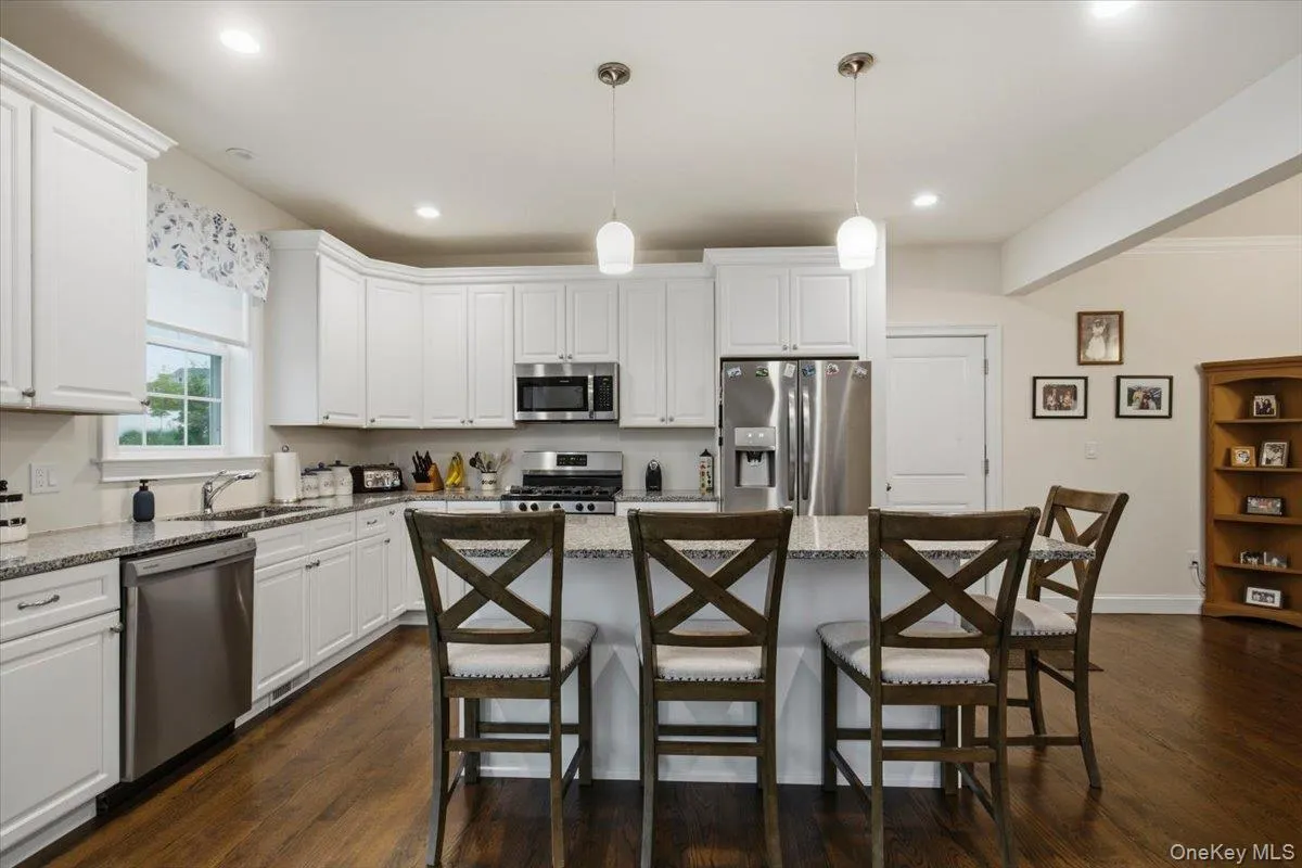 Kitchen featuring white cabinetry, stainless steel appliances, speckled stone countertops, and an island with pendant lighting Kitchen featuring white cabinetry, stainless steel appliances, speckled stone countertops, and an island with pendant lighting