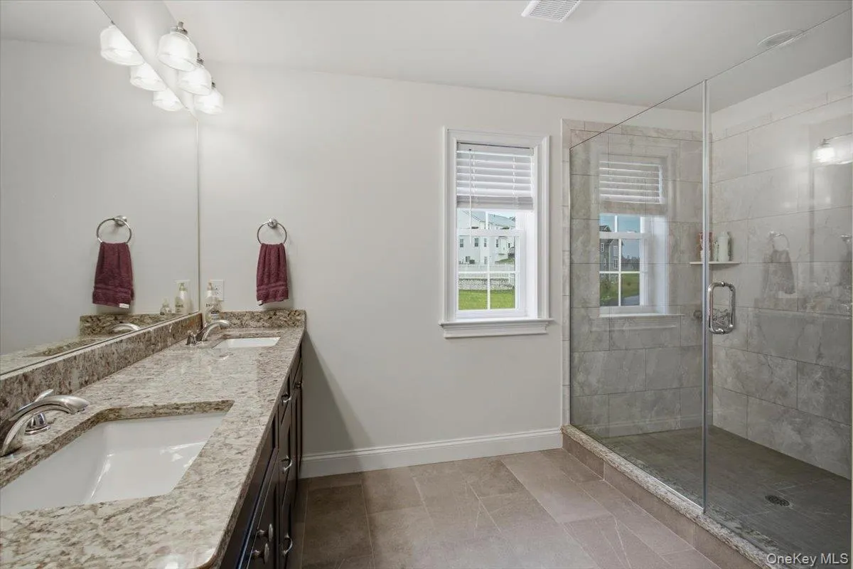 Dual vanity with light-toned countertop, dark wood-finish cabinetry, chrome fixtures and large walk in shower Dual vanity with light-toned countertop, dark wood-finish cabinetry, chrome fixtures and large walk in shower