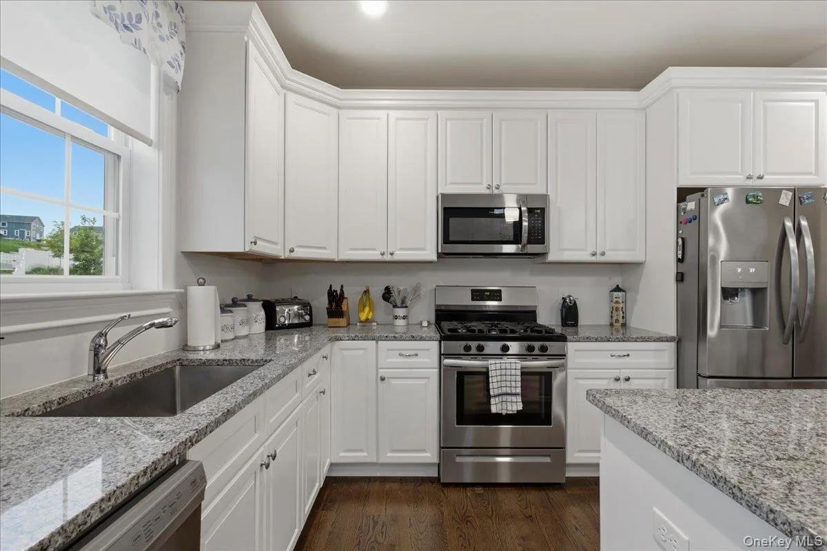 White cabinetry with crown molding, stainless steel appliances, granite countertops, single basin stainless steel sink, and wood-finish flooring White cabinetry with crown molding, stainless steel appliances, granite countertops, single basin stainless steel sink, and wood-finish flooring