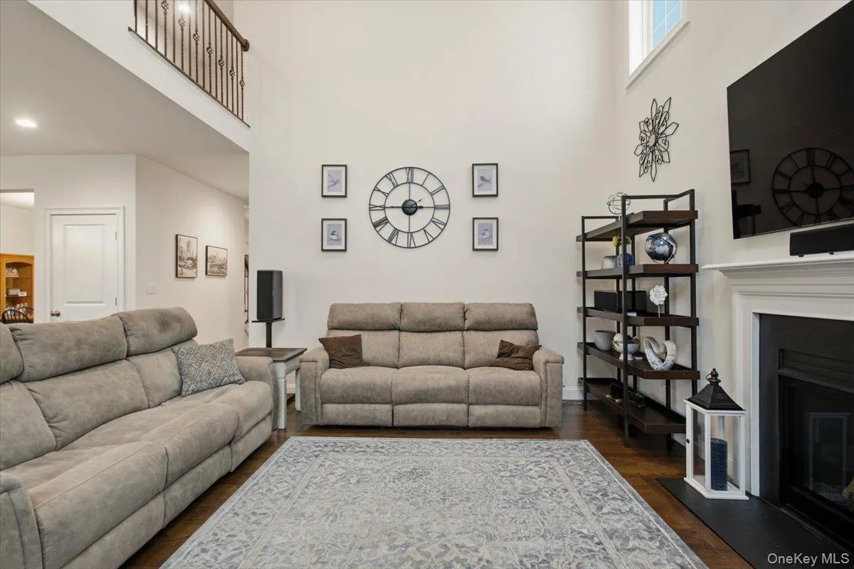 Vaulted ceiling with upper-level window, built-in fireplace with white mantel, dark wood-finish flooring, and an upper-level railing with decorative balusters Vaulted ceiling with upper-level window, built-in fireplace with white mantel, dark wood-finish flooring, and an upper-level railing with decorative balusters