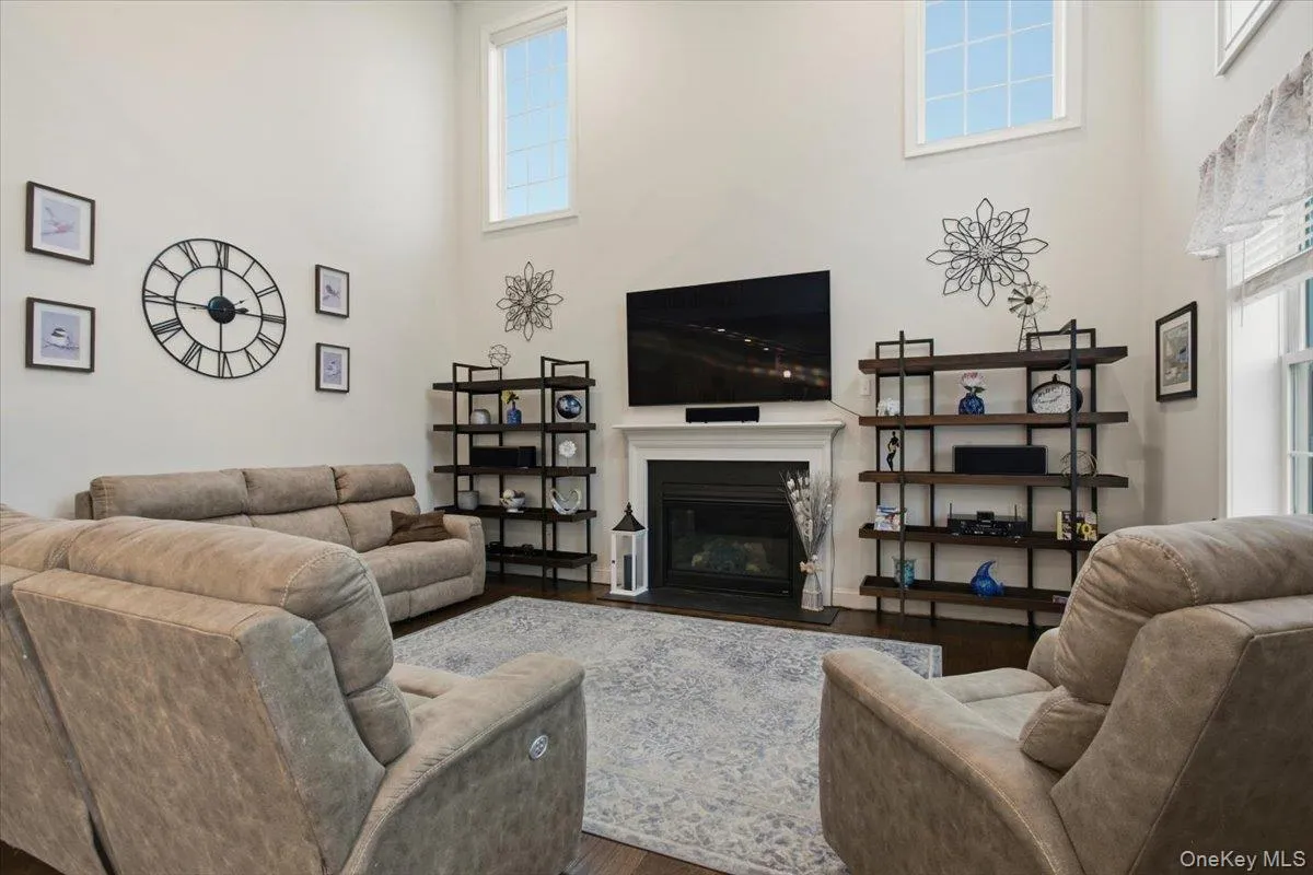 Double-height ceiling, fireplace with white mantel, dark wood-finish flooring, and high transom windows Double-height ceiling, fireplace with white mantel, dark wood-finish flooring, and high transom windows