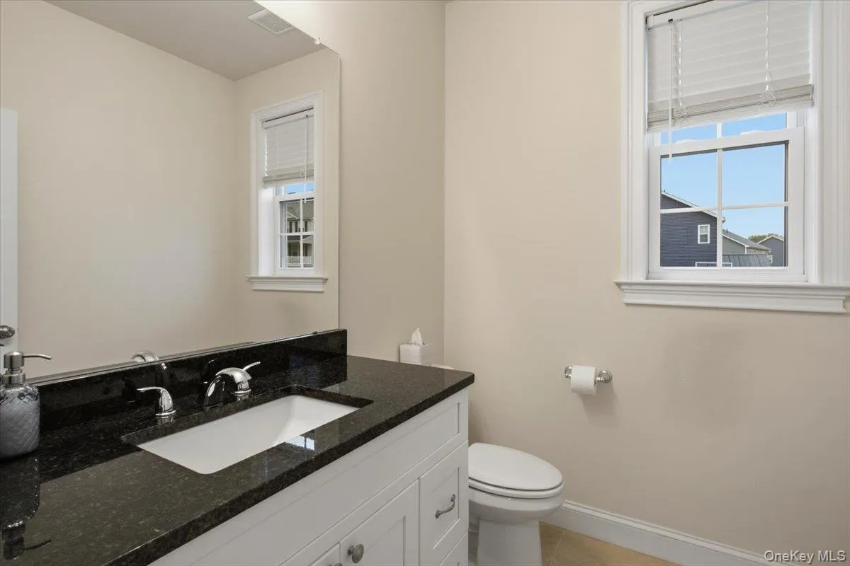 1st floor half bath, white vanity with under-mount sink, dark countertop, chrome faucet, and mirrored wall 1st floor half bath, white vanity with under-mount sink, dark countertop, chrome faucet, and mirrored wall