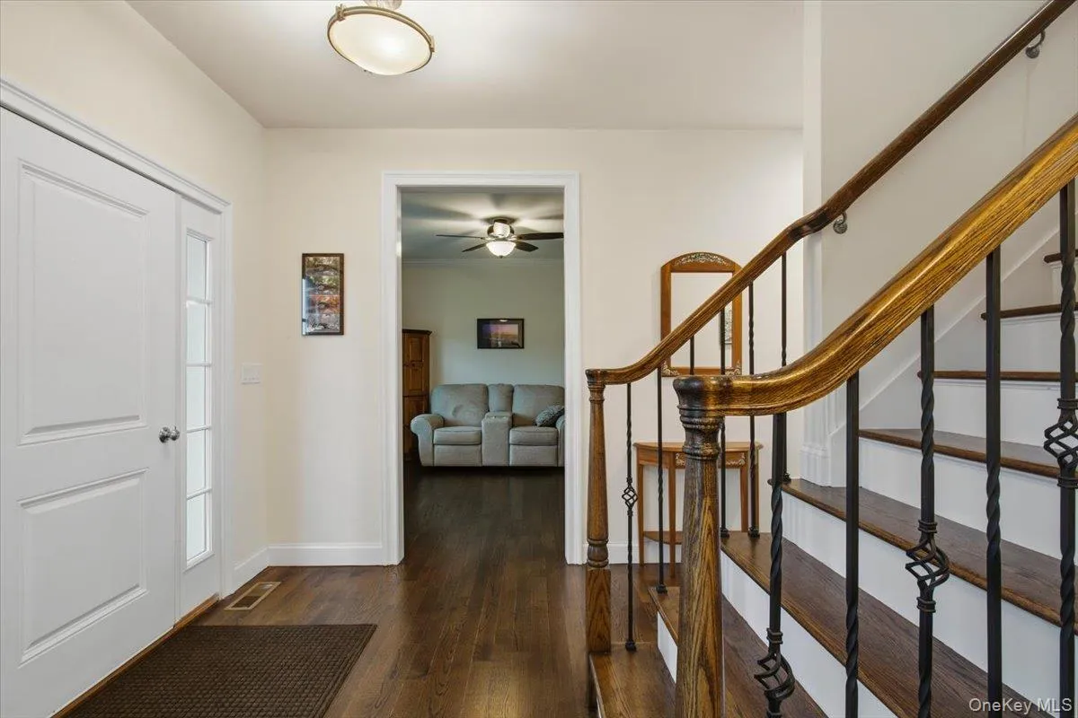 Foyer featuring wood-finish flooring, a white paneled entry door, a sidelight window, a semi-flush mount ceiling light, and a staircase with wood handrails and wrought iron balusters Foyer featuring wood-finish flooring, a white paneled entry door, a sidelight window, a semi-flush mount ceiling light, and a staircase with wood handrails and wrought iron balusters