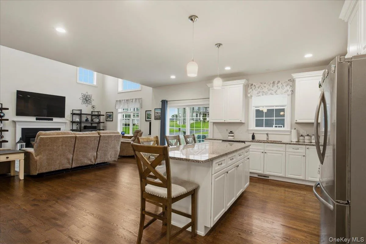 Open-concept living area with wood-finish flooring, a white kitchen island with a granite countertop, white cabinetry, and stainless steel appliances Open-concept living area with wood-finish flooring, a white kitchen island with a granite countertop, white cabinetry, and stainless steel appliances