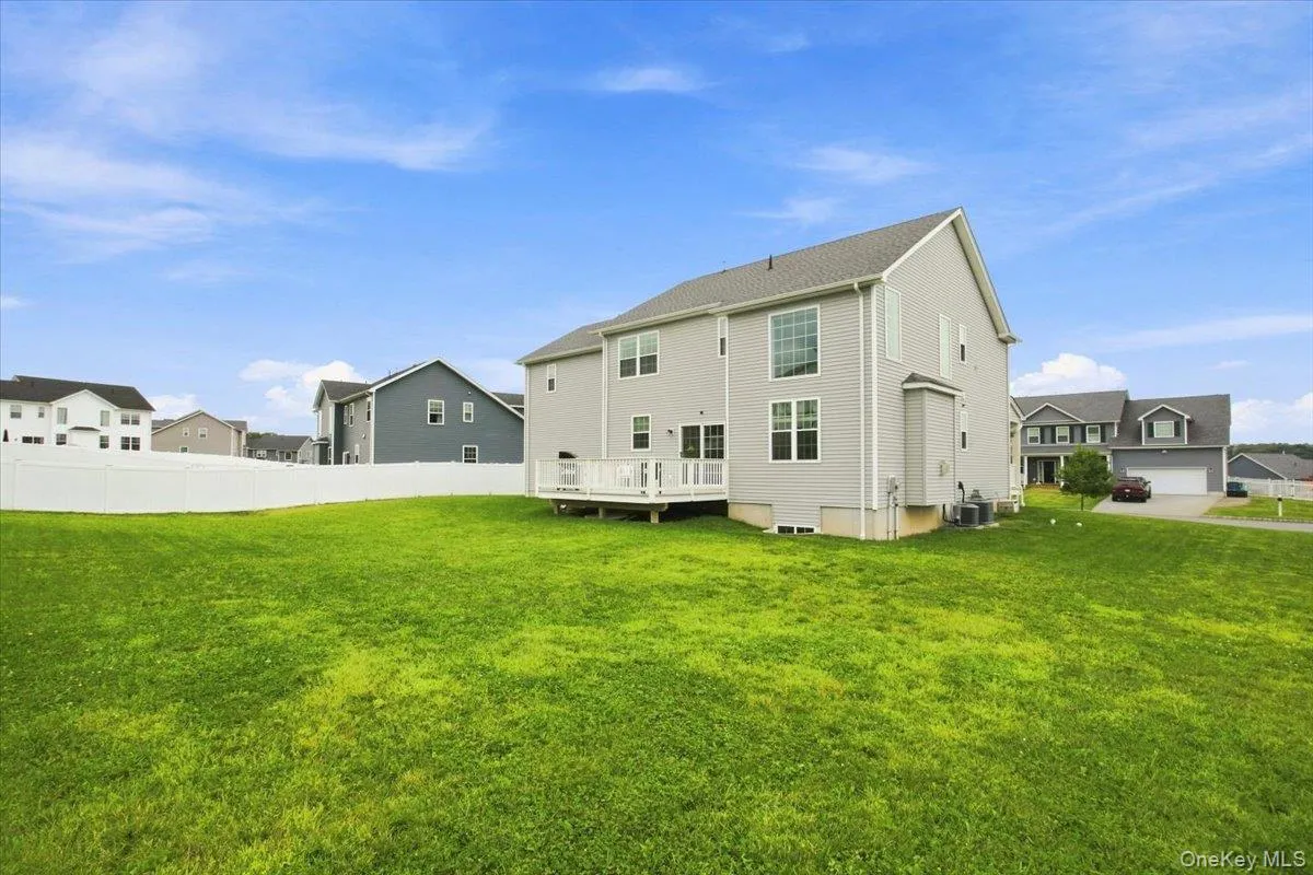 Spacious rear yard with green grass, white privacy fencing, and a ground-level deck Spacious rear yard with green grass, white privacy fencing, and a ground-level deck