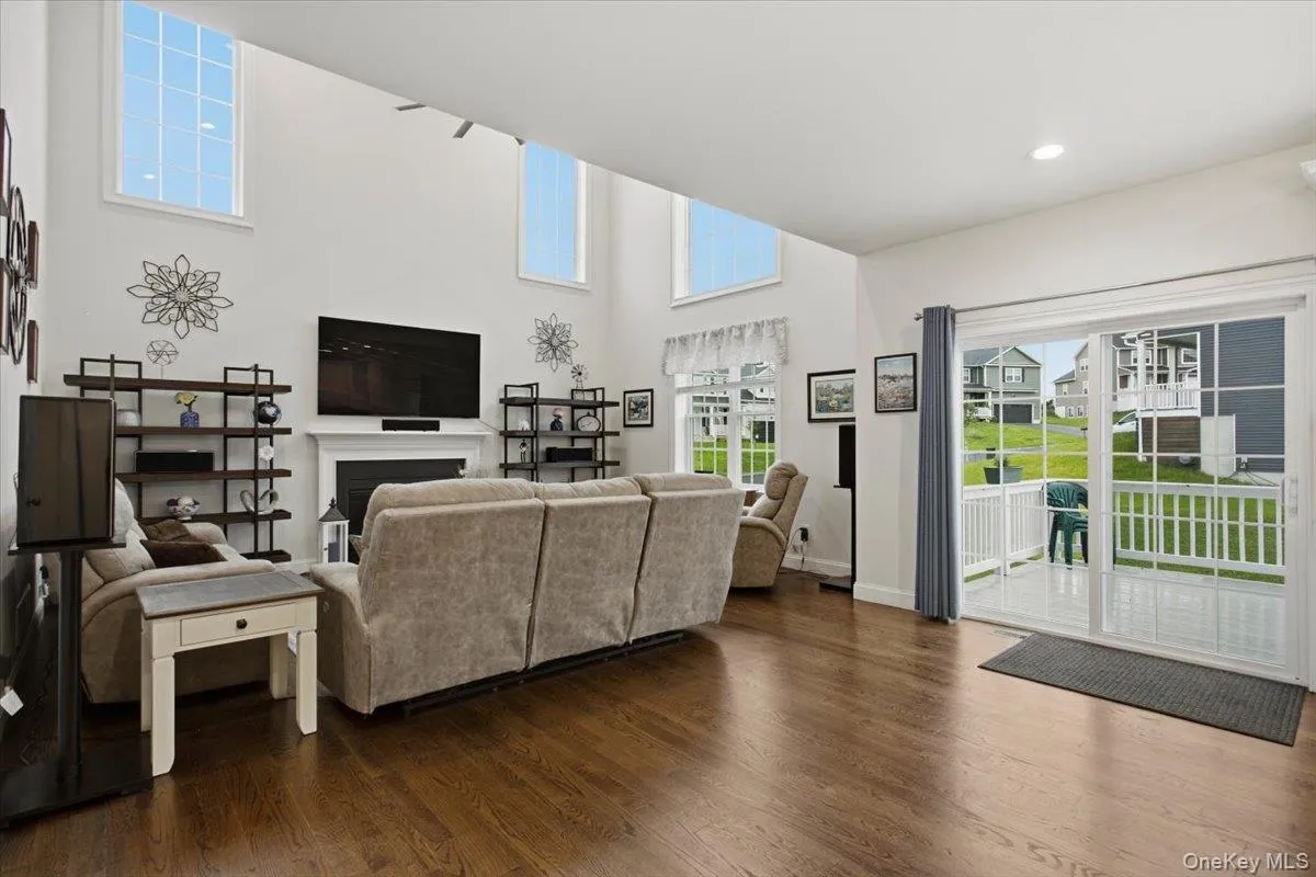 Two-story living area featuring wood-finish flooring, a white mantel fireplace, and high-set windows Two-story living area featuring wood-finish flooring, a white mantel fireplace, and high-set windows