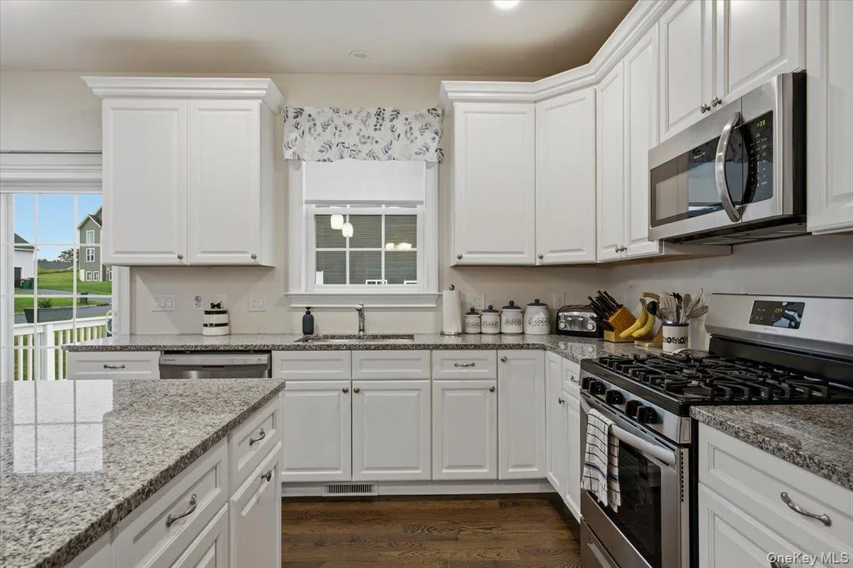 Kitchen featuring white cabinetry, light-toned granite countertops, and stainless steel appliances Kitchen featuring white cabinetry, light-toned granite countertops, and stainless steel appliances