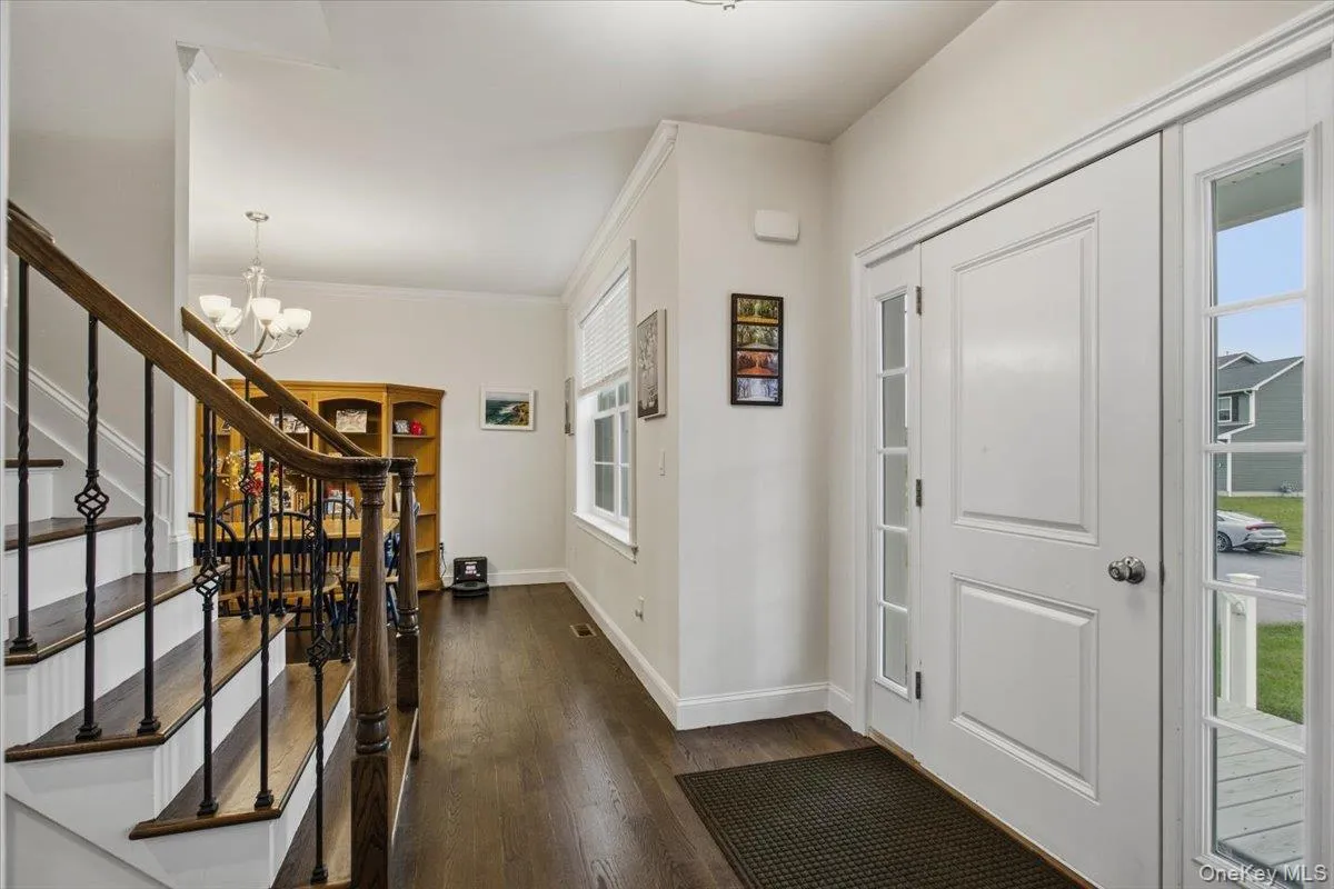 Entryway featuring wood-finish flooring, a staircase with dark wood handrails and wrought iron balusters, and a white paneled door with glass sidelights Entryway featuring wood-finish flooring, a staircase with dark wood handrails and wrought iron balusters, and a white paneled door with glass sidelights