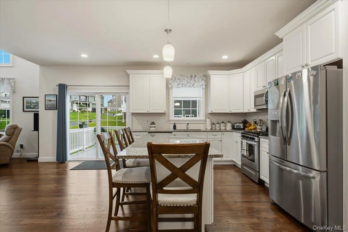 Kitchen featuring white cabinetry, stainless steel appliances, a center island with seating, pendant lighting, and wood-finish flooring Kitchen featuring white cabinetry, stainless steel appliances, a center island with seating, pendant lighting, and wood-finish flooring