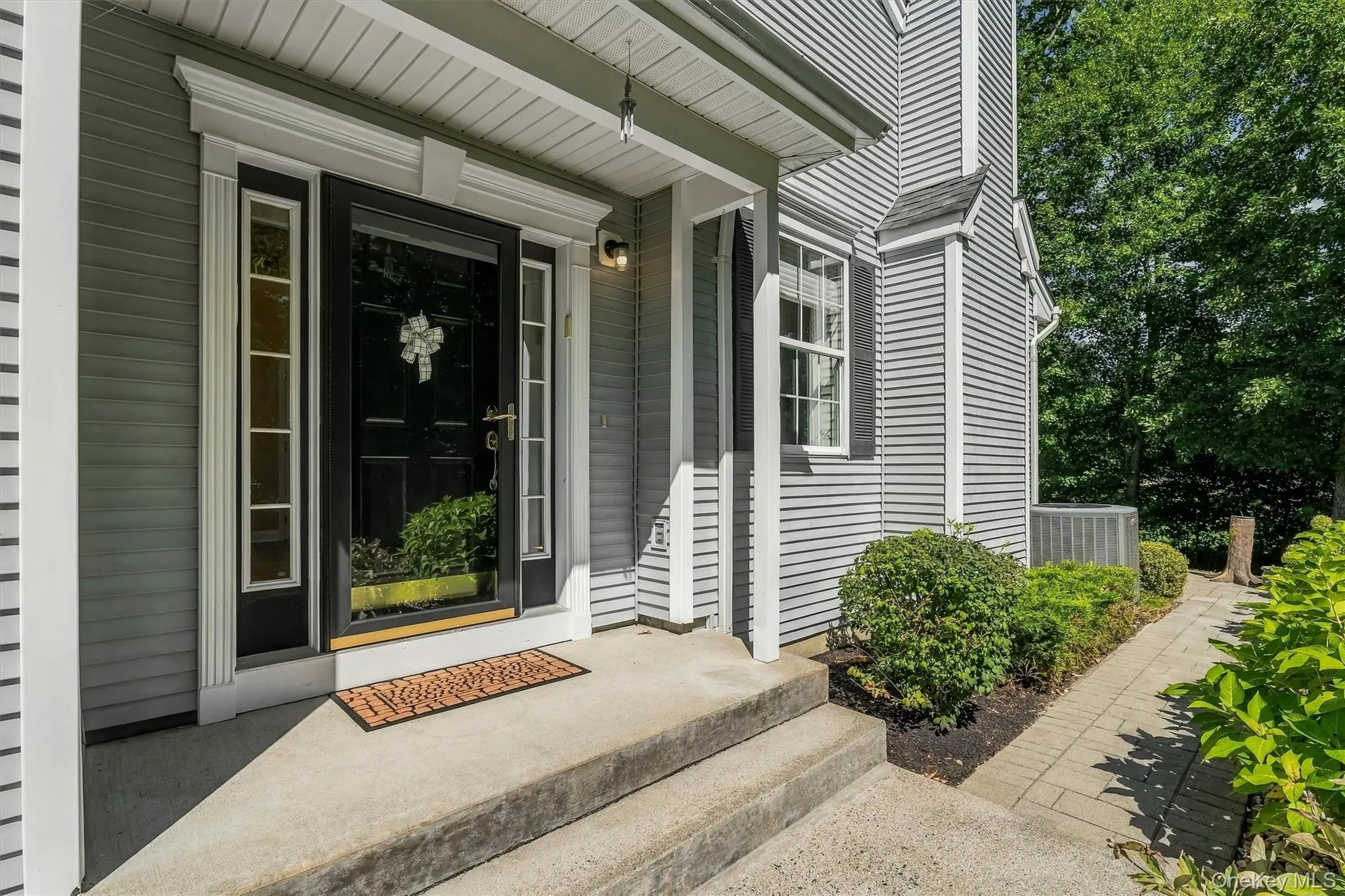 Paneled front door with sidelight windows, covered entry, concrete steps, horizontal siding, and a paver walkway Paneled front door with sidelight windows, covered entry, concrete steps, horizontal siding, and a paver walkway