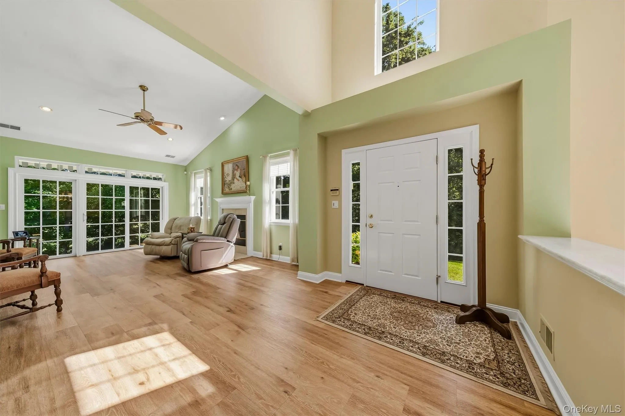 Vaulted ceiling with recessed lighting, wood-finish flooring, white fireplace, multiple large windows, and a front entry door with sidelights Vaulted ceiling with recessed lighting, wood-finish flooring, white fireplace, multiple large windows, and a front entry door with sidelights