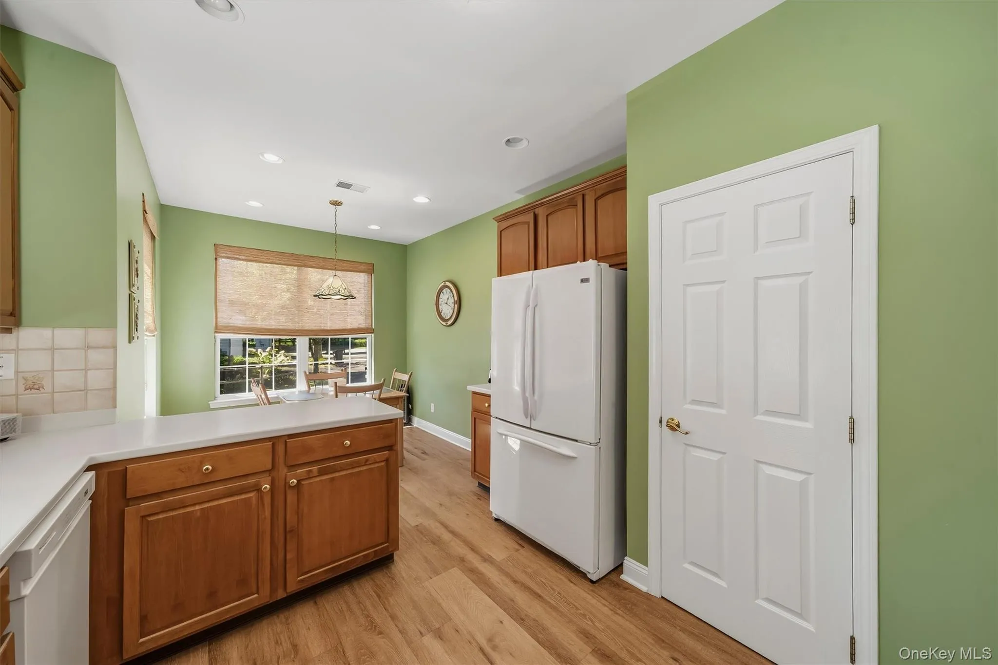 Kitchen featuring wood-finish flooring, wood cabinetry with gold-tone hardware, a tiled backsplash, and recessed lighting Kitchen featuring wood-finish flooring, wood cabinetry with gold-tone hardware, a tiled backsplash, and recessed lighting