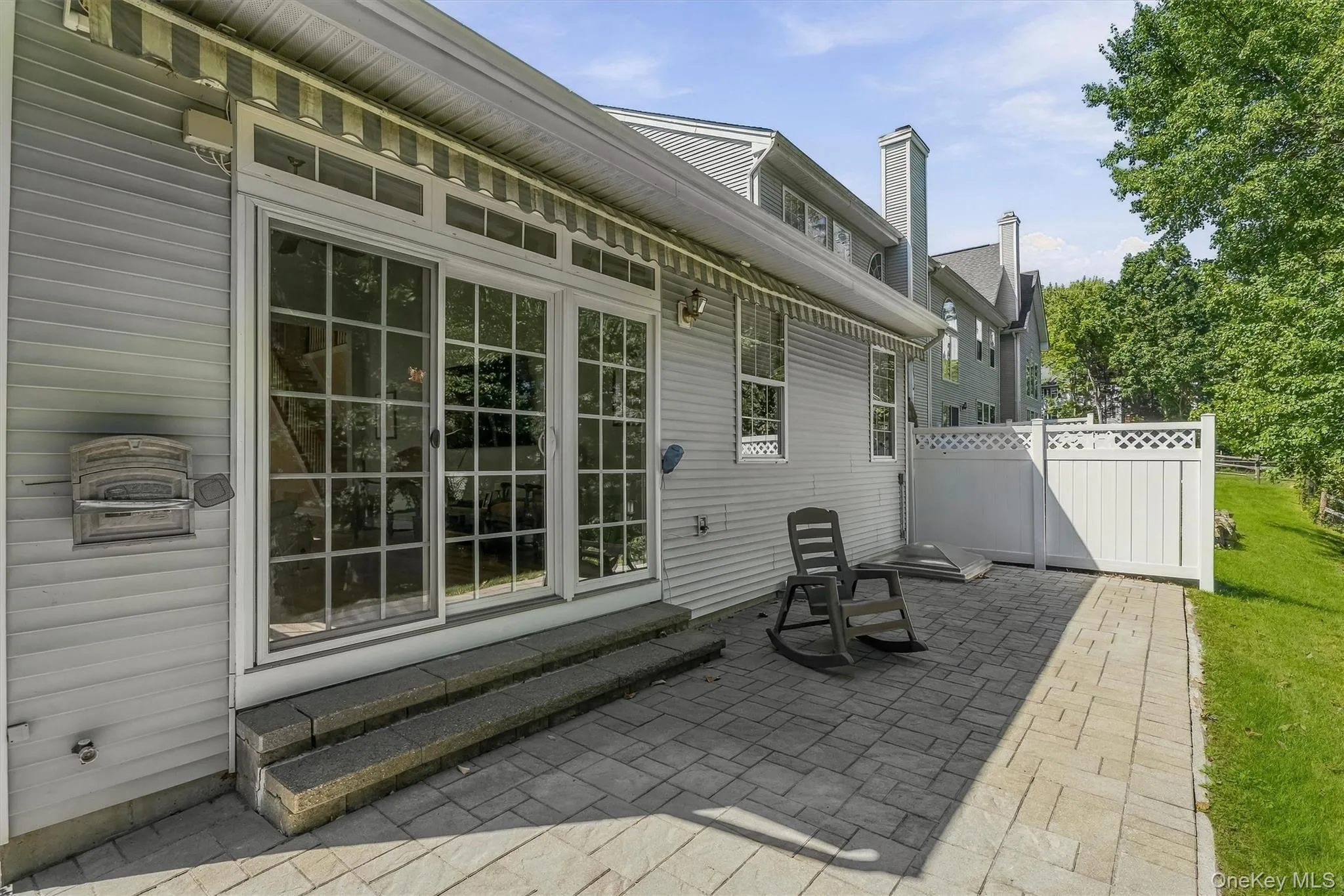 Paved patio with white privacy fencing, sliding glass doors with transom windows, and a retractable awning Paved patio with white privacy fencing, sliding glass doors with transom windows, and a retractable awning