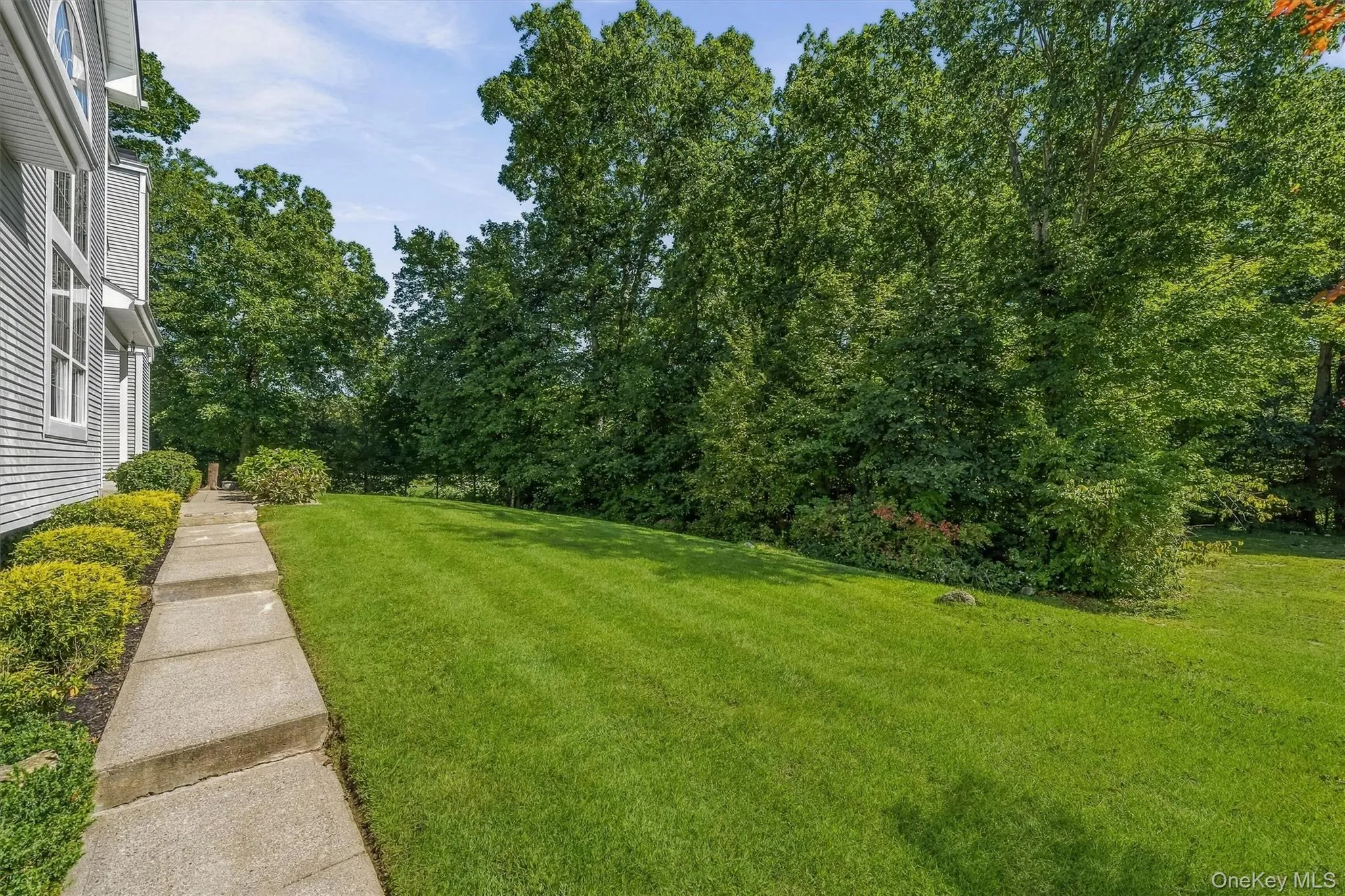 Expansive lawn with mature trees and established landscaping, bordered by a concrete walkway and a shingled exterior Expansive lawn with mature trees and established landscaping, bordered by a concrete walkway and a shingled exterior