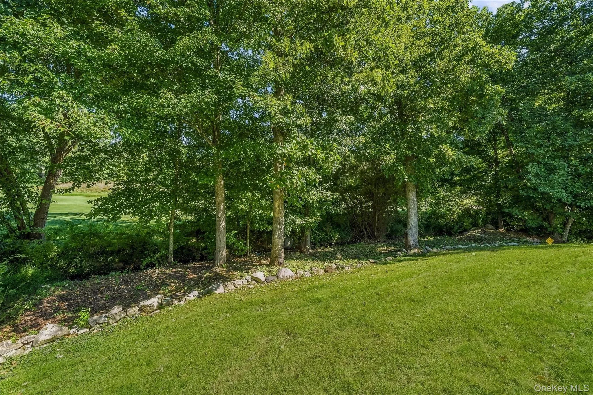 Expansive green lawn with a natural stone retaining wall and mature trees Expansive green lawn with a natural stone retaining wall and mature trees