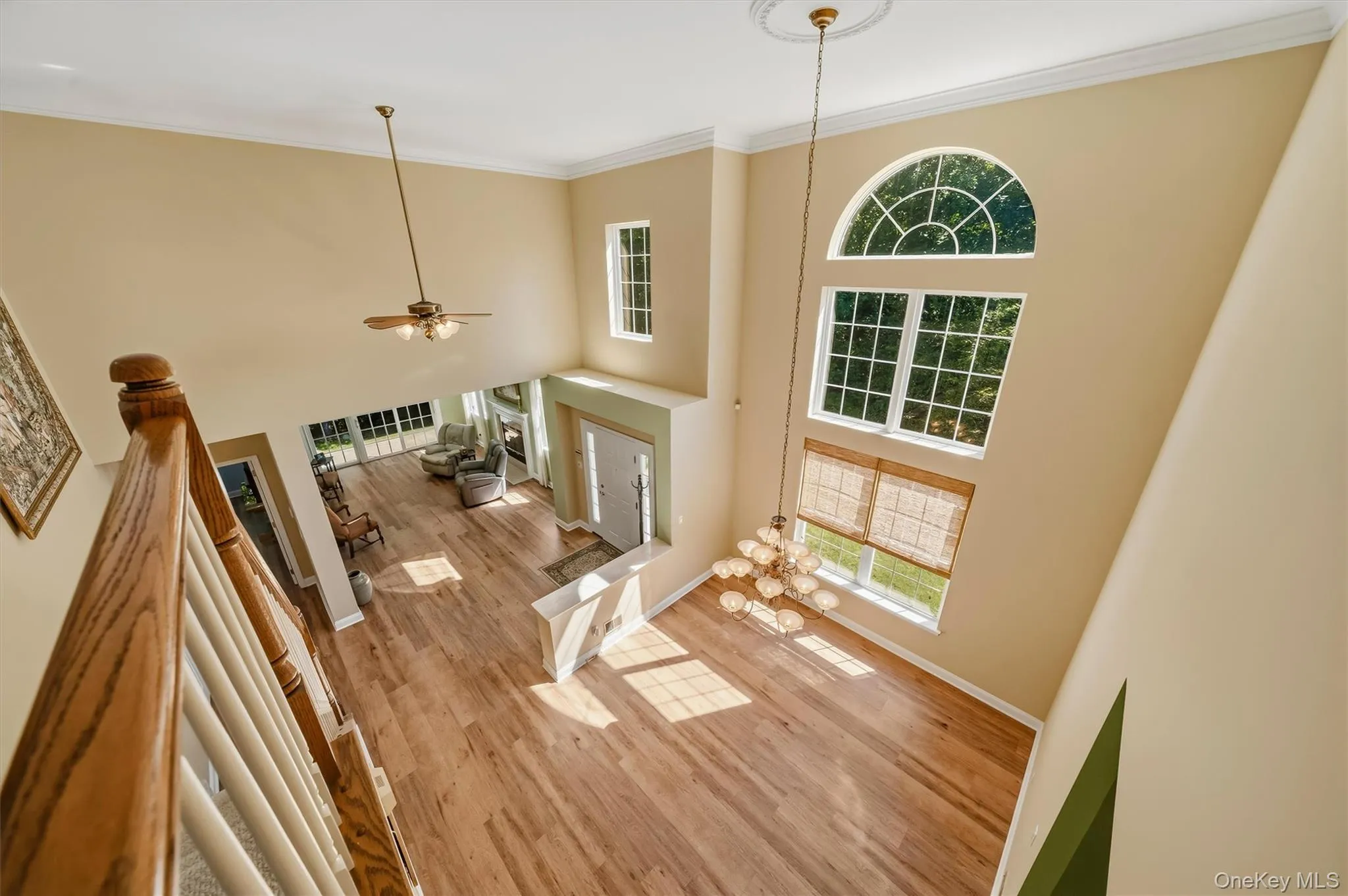 Two-story foyer featuring wood-finish flooring, a tiered window arrangement with an arched transom, an ornate chandelier, and a ceiling fan Two-story foyer featuring wood-finish flooring, a tiered window arrangement with an arched transom, an ornate chandelier, and a ceiling fan