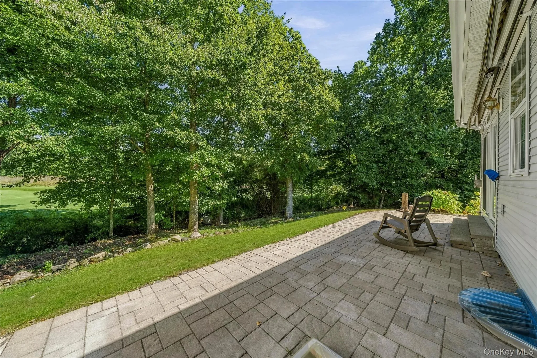 Paver patio with a stone retaining wall, adjacent to a sloped lawn and mature trees Paver patio with a stone retaining wall, adjacent to a sloped lawn and mature trees