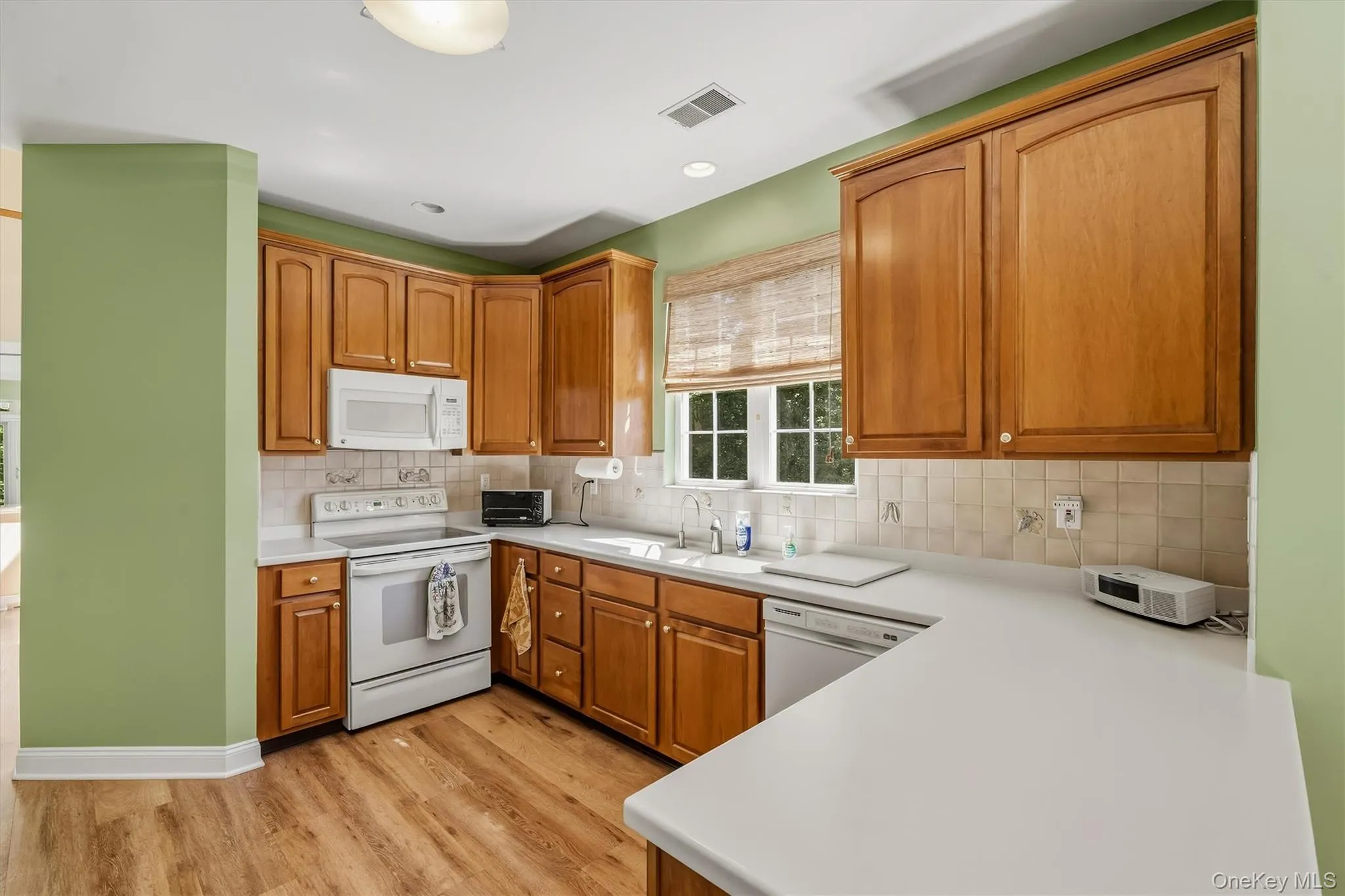 U-shaped kitchen featuring wood-finish cabinetry, white appliances, a double basin sink, and wood-finish flooring U-shaped kitchen featuring wood-finish cabinetry, white appliances, a double basin sink, and wood-finish flooring