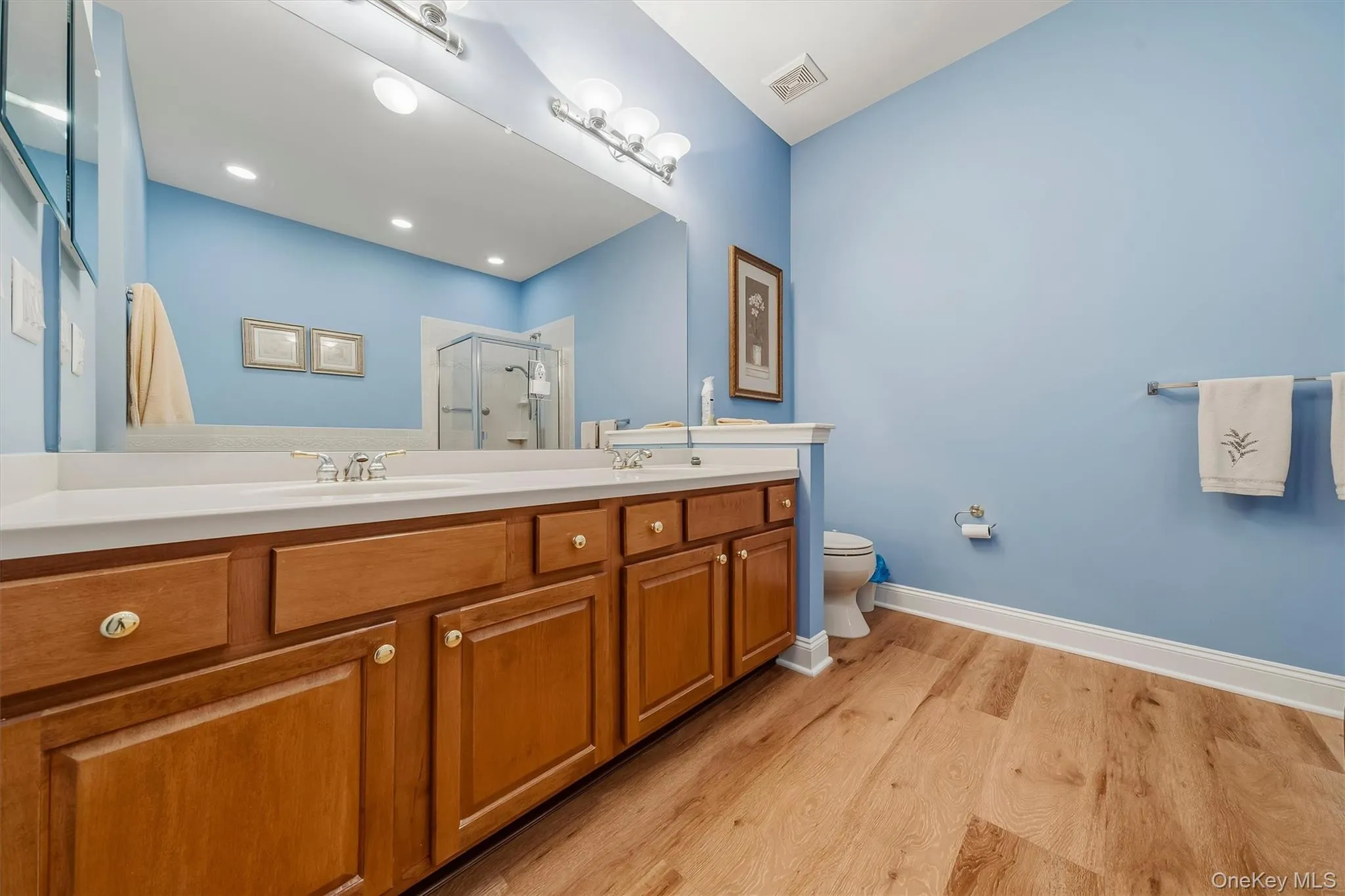 Double vanity with wood-finish cabinetry, white countertop, and dual sinks Double vanity with wood-finish cabinetry, white countertop, and dual sinks