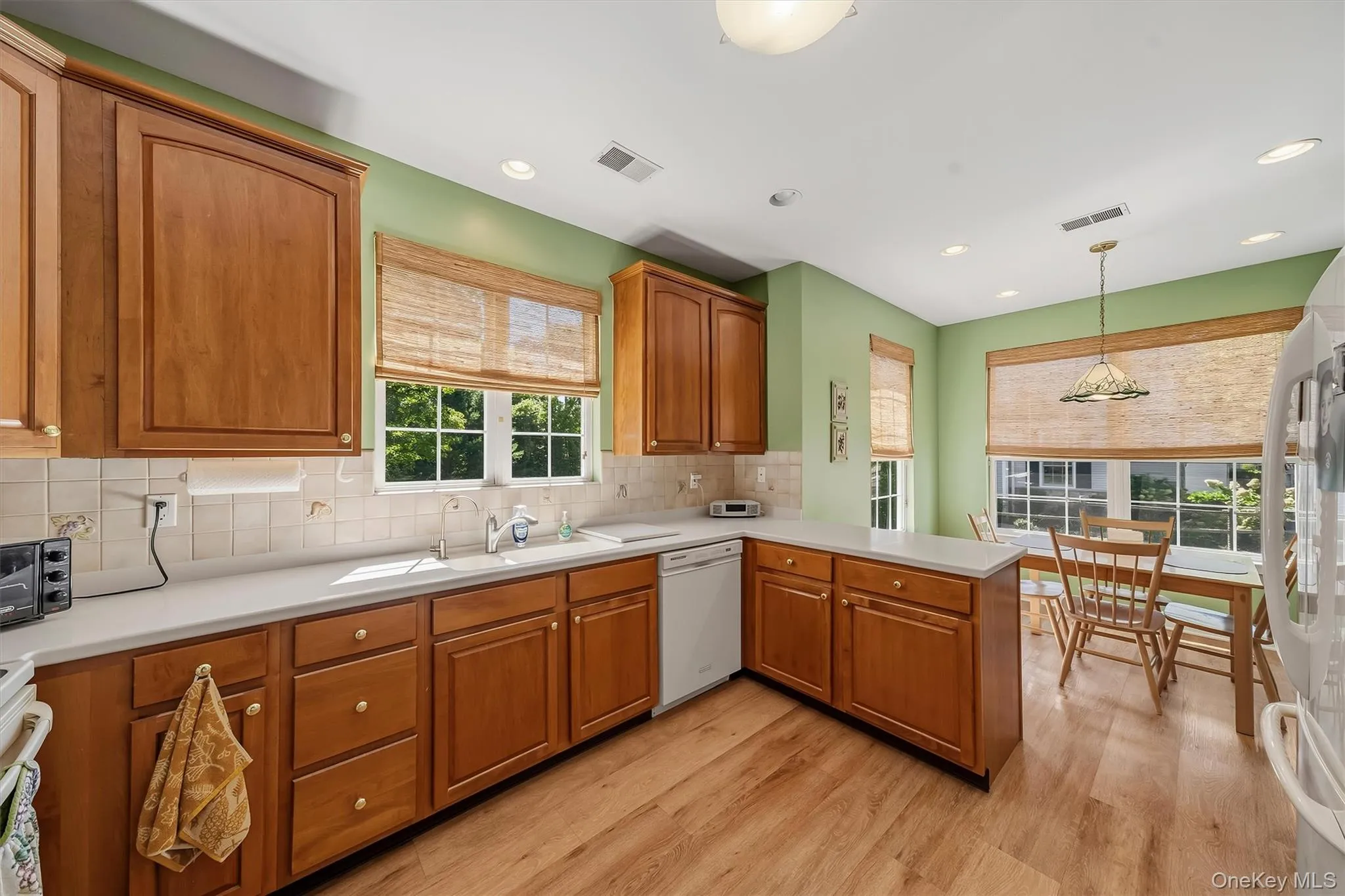 Wood-finish flooring, wood cabinetry, white countertops, tile backsplash, and recessed lighting Wood-finish flooring, wood cabinetry, white countertops, tile backsplash, and recessed lighting