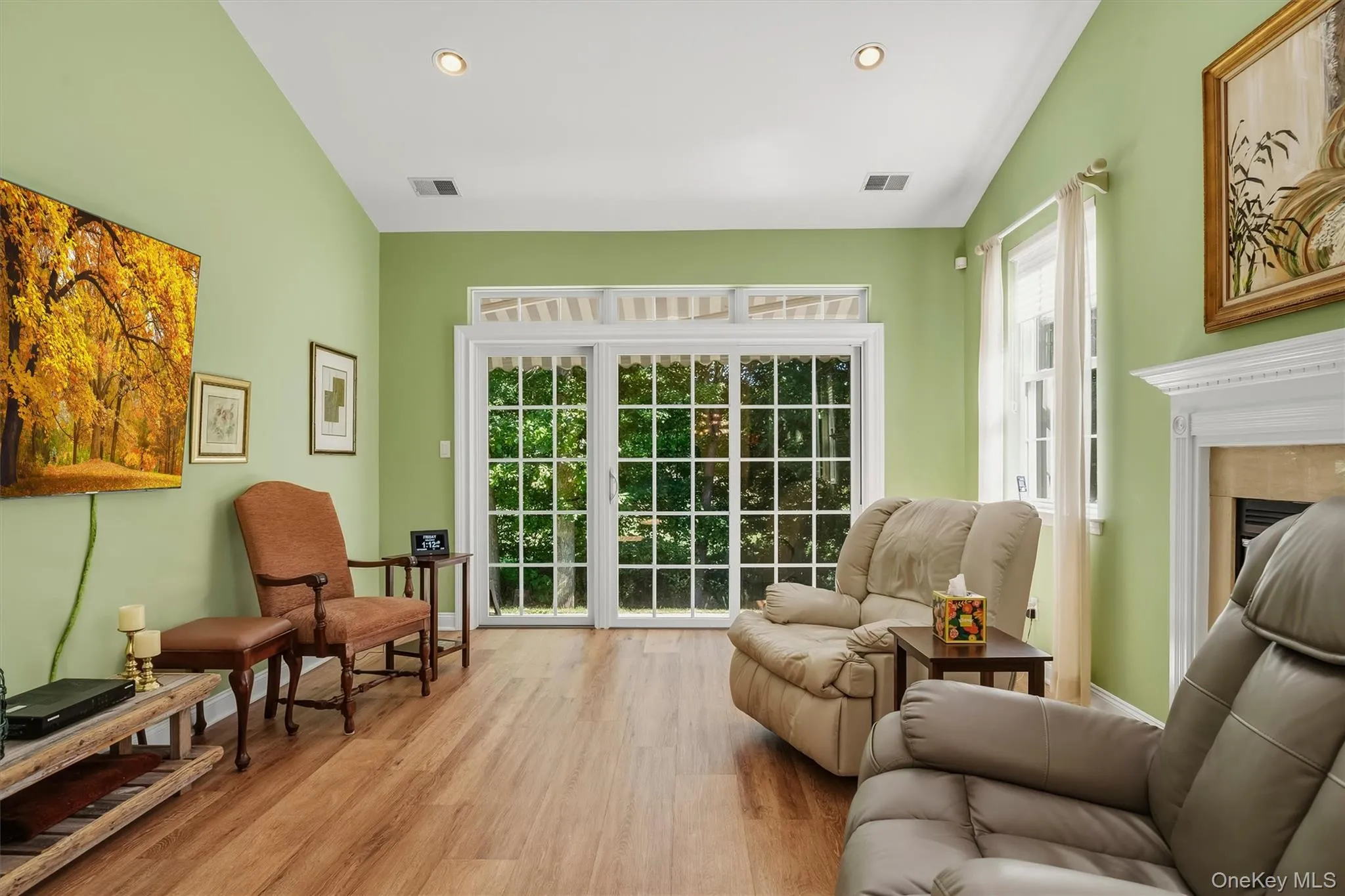 Wood-finish flooring throughout, recessed ceiling lighting, a fireplace with a white mantel, and a sliding glass door with transom windows Wood-finish flooring throughout, recessed ceiling lighting, a fireplace with a white mantel, and a sliding glass door with transom windows