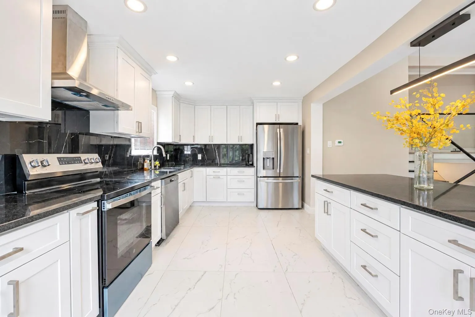 Kitchen featuring white cabinetry, black countertops, stainless steel appliances, a range hood, and recessed lighting Kitchen featuring white cabinetry, black countertops, stainless steel appliances, a range hood, and recessed lighting