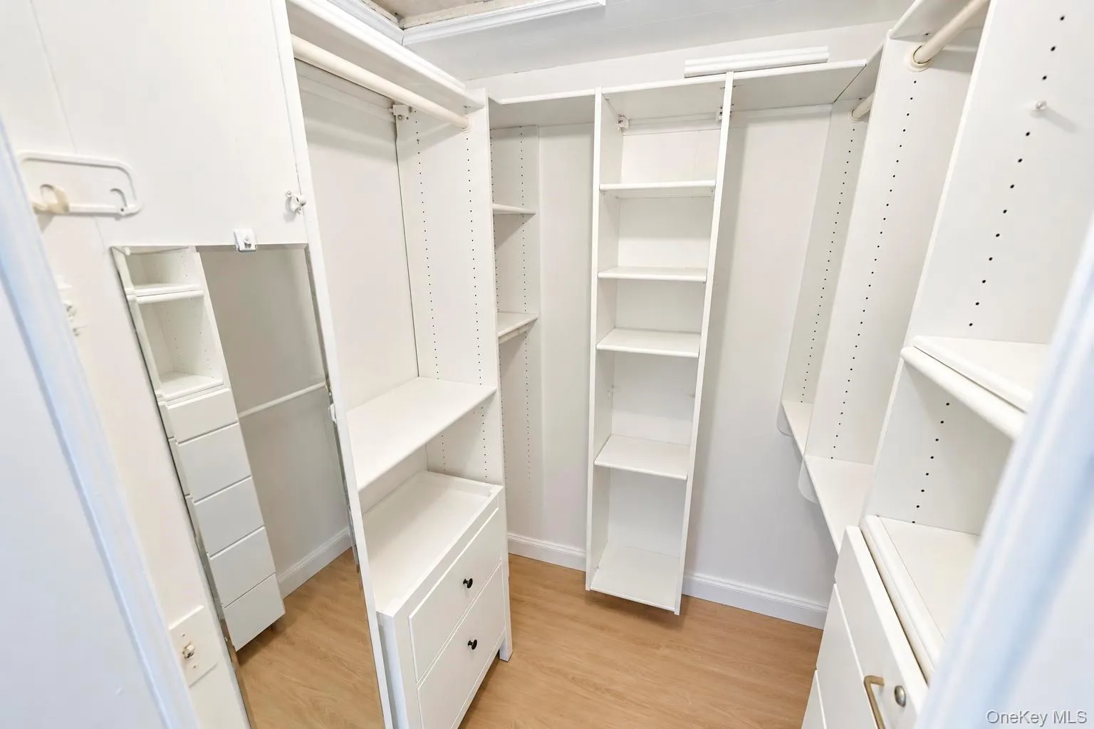 Walk-in closet featuring white built-in shelving, hanging rods, and integrated drawers Walk-in closet featuring white built-in shelving, hanging rods, and integrated drawers