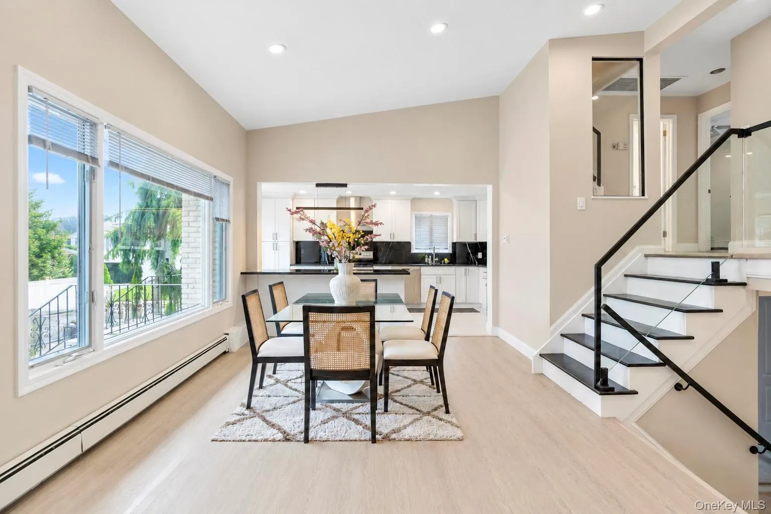 Vaulted ceilings, expansive windows, wood-finish flooring, open-concept kitchen, and a staircase with glass railing Vaulted ceilings, expansive windows, wood-finish flooring, open-concept kitchen, and a staircase with glass railing